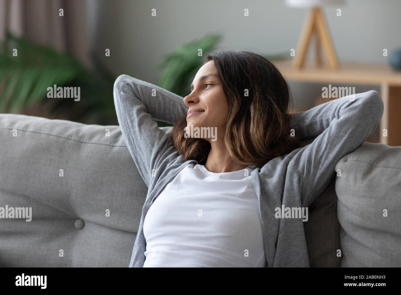 Woman put hands behind head leaned on couch resting indoors Stock Photo