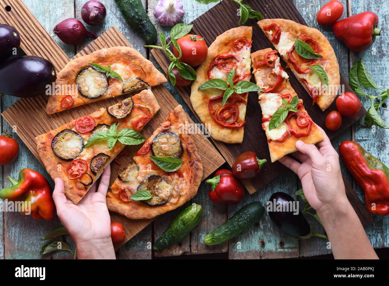 Slender woman hands reaching for healthy vegetarian pizza. Homemade rustic pizzas with aubergines, bell peppers, basil and tomatoes on oak boards with Stock Photo