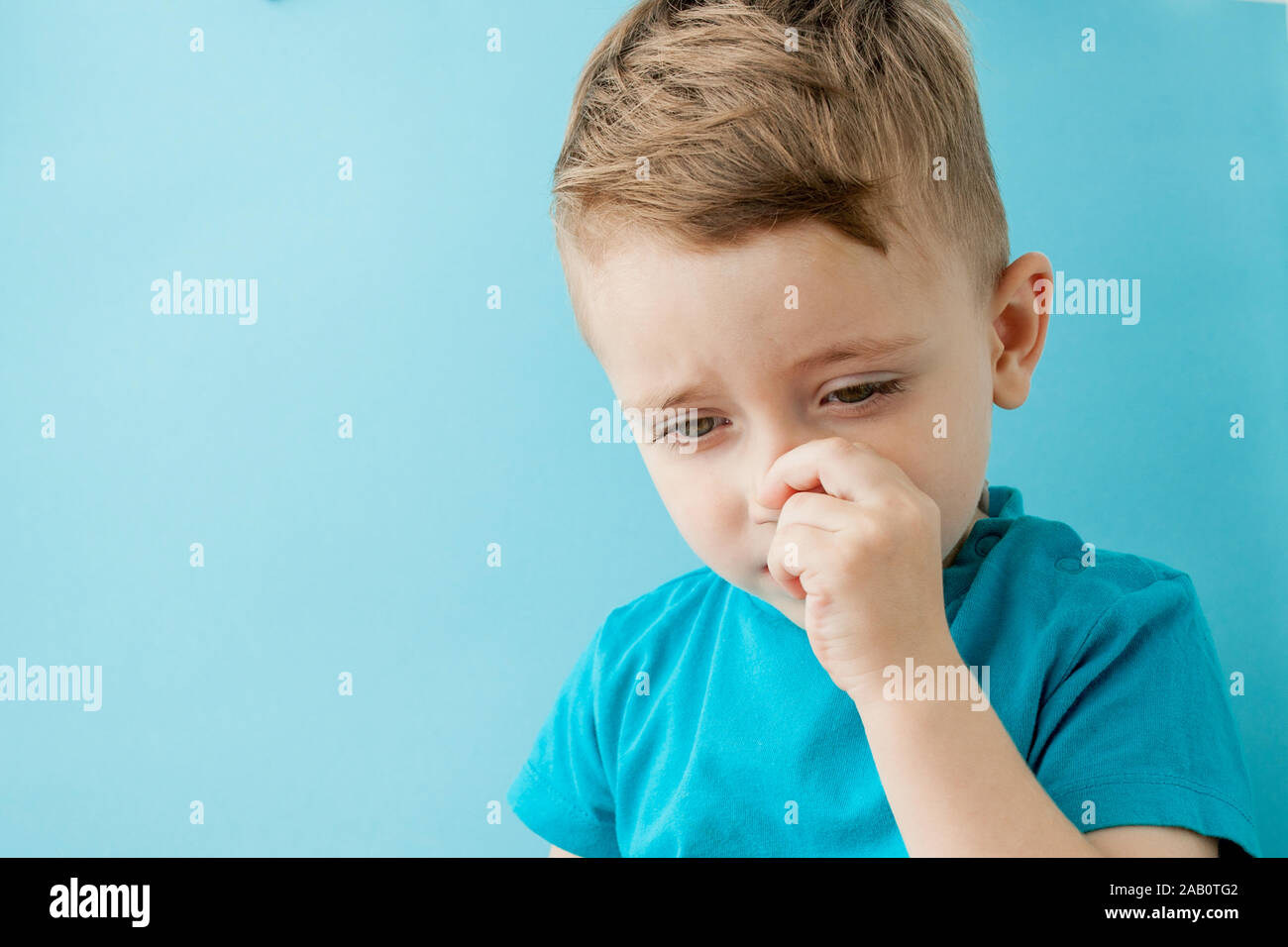 Little caucasian boy picking his nose on blue background. Stock Photo
