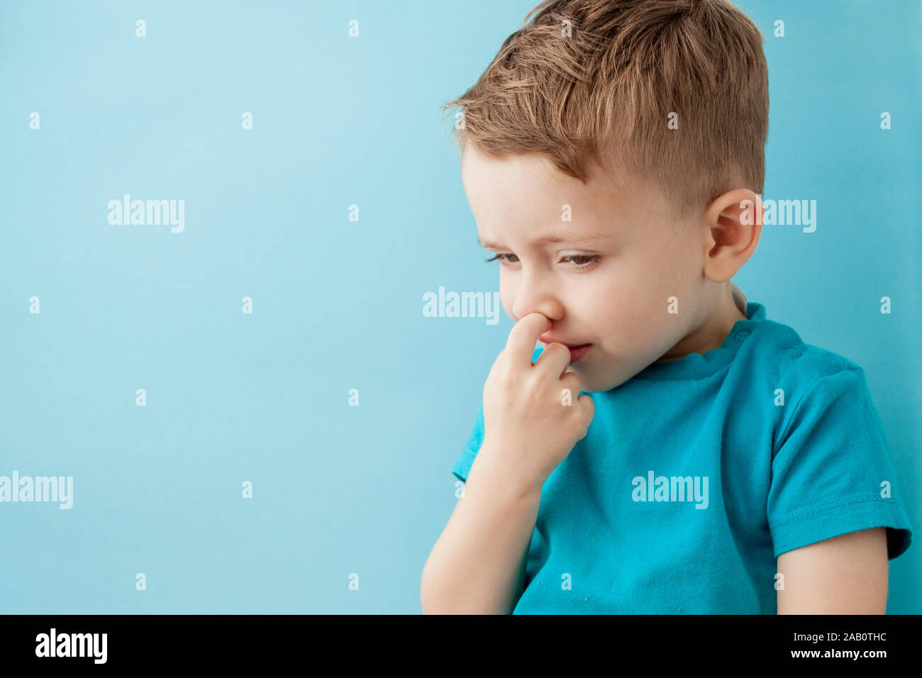 Little caucasian boy picking his nose on blue background. Stock Photo