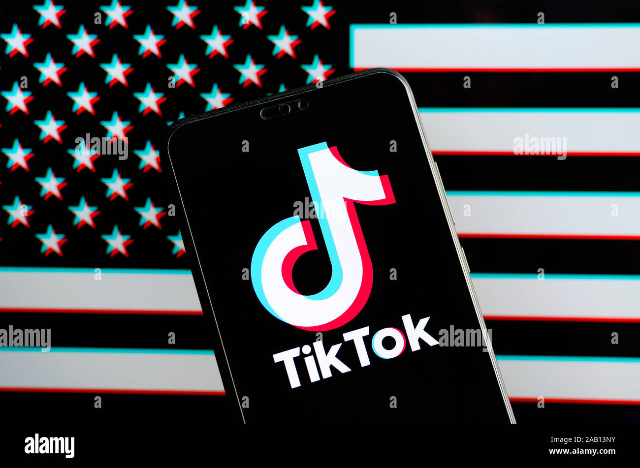 TikTok app logo on the smartphone and a blurred american flag with RGB-split effect on the laptop screen behind it. Strong concept photo. Stock Photo