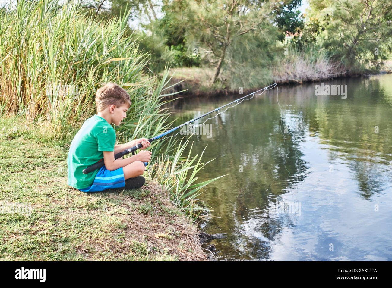 Young person, boy aged 6, sitting with legs crossed fishing from the bank of a pond in Queensland Australia.. Stock Photo