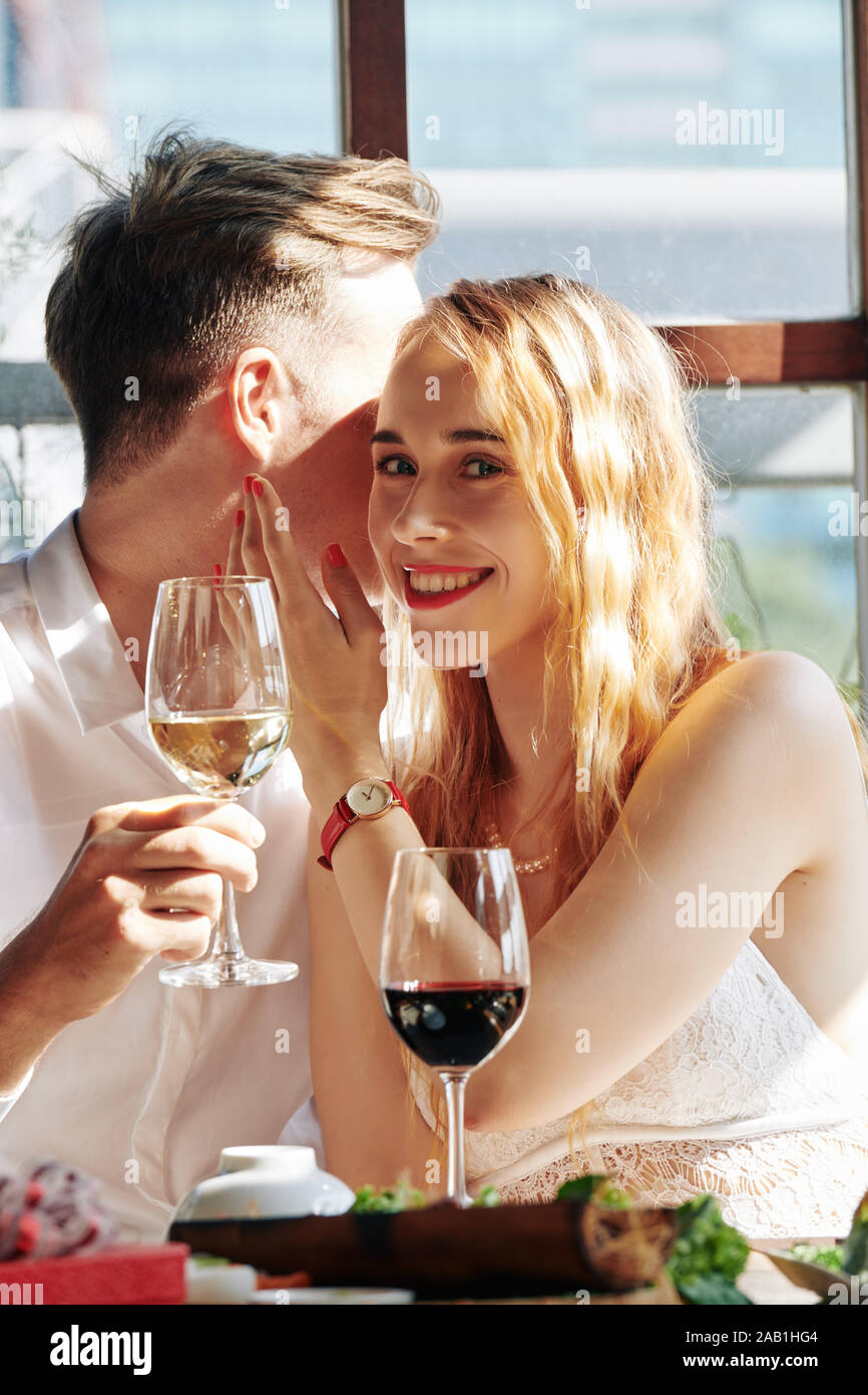 Beautiful young smiling woman drinking wine with her boyfriend and listening to him telling compliments Stock Photo
