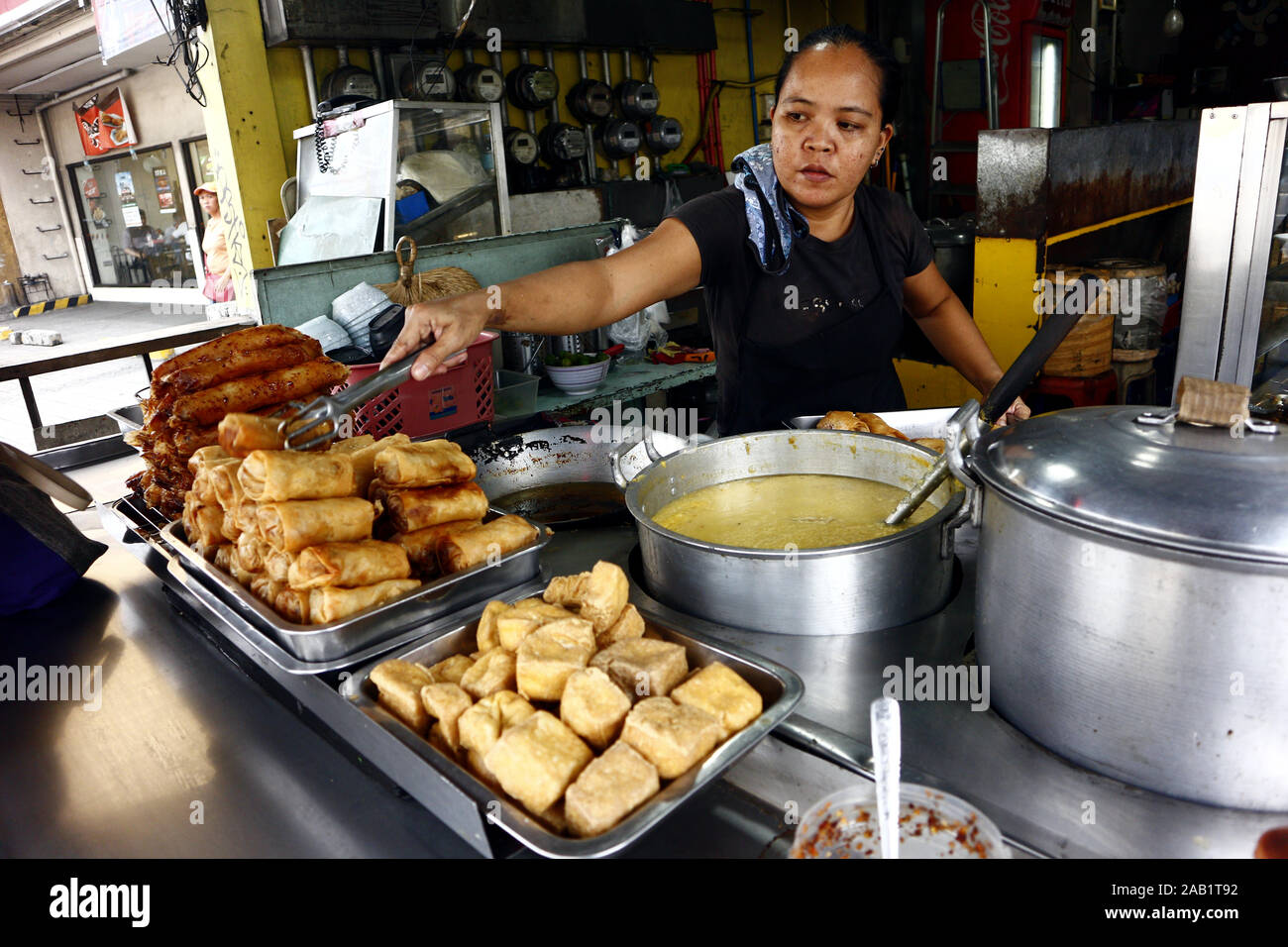 Cainta, Rizal, Philippines – November 23, 2019: Worker at a neighborhood eatery or carinderia serves cooked food to a customer. Stock Photo