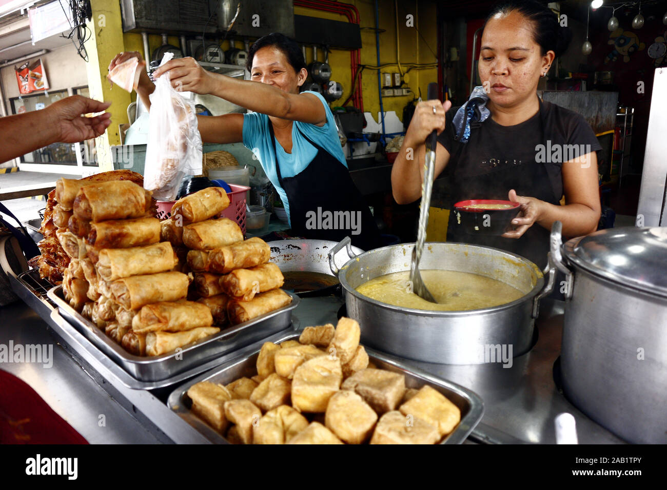 Cainta, Rizal, Philippines – November 23, 2019: Worker at a neighborhood eatery or carinderia serves cooked food to a customer. Stock Photo