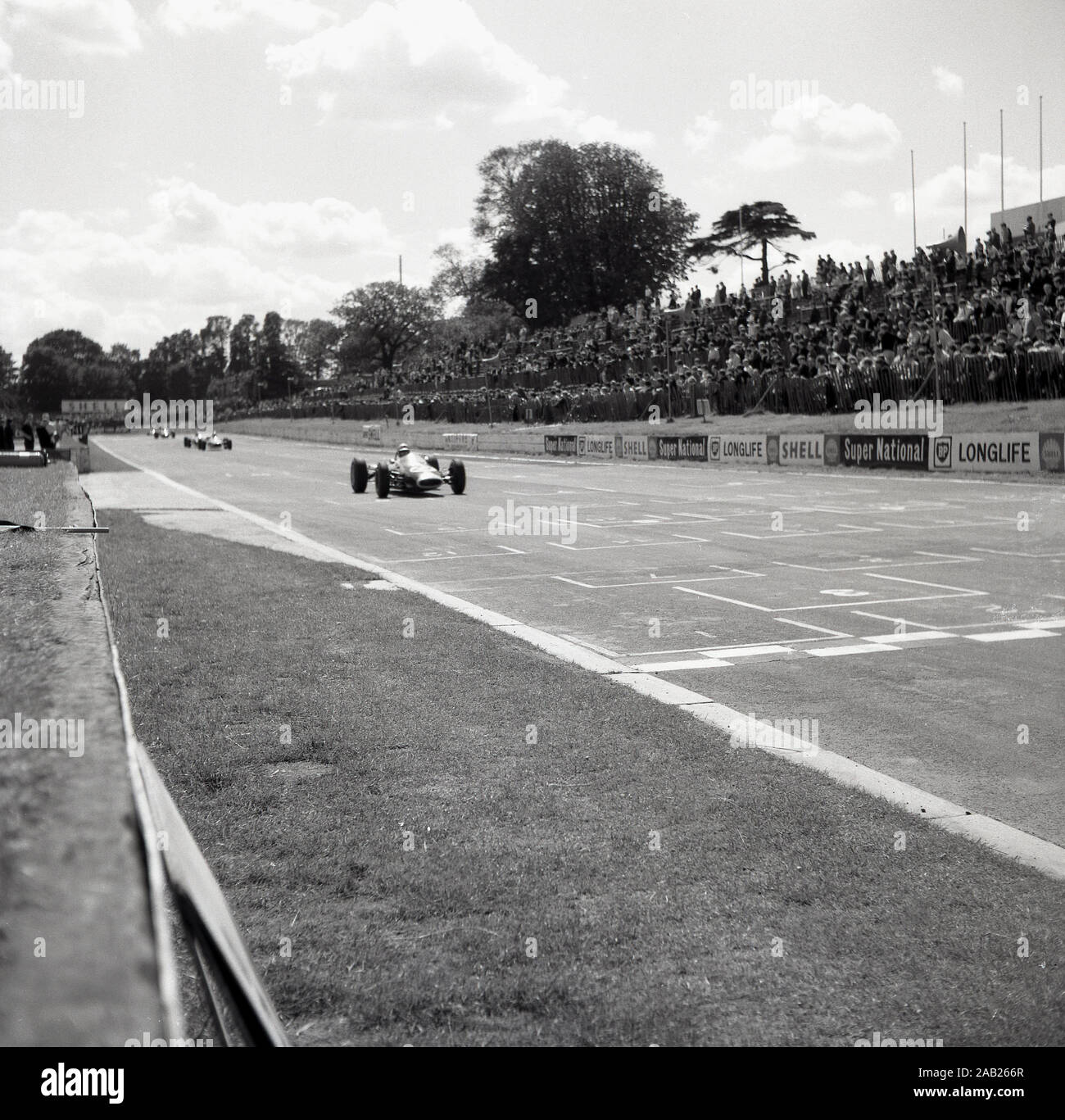 1960s, historical, motor racing at the Crystal Palace race circuit in Crystal Palace park in South London, London, England, UK, a car comes down the finishing straight watched by a crowd of spectators. Stock Photo