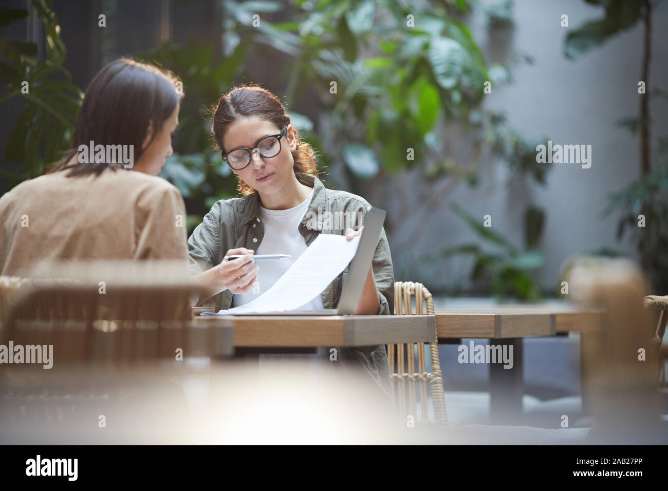Portrait of two female entrepreneurs discussing project while working at table in outdoor cafe terrace, copy space Stock Photo