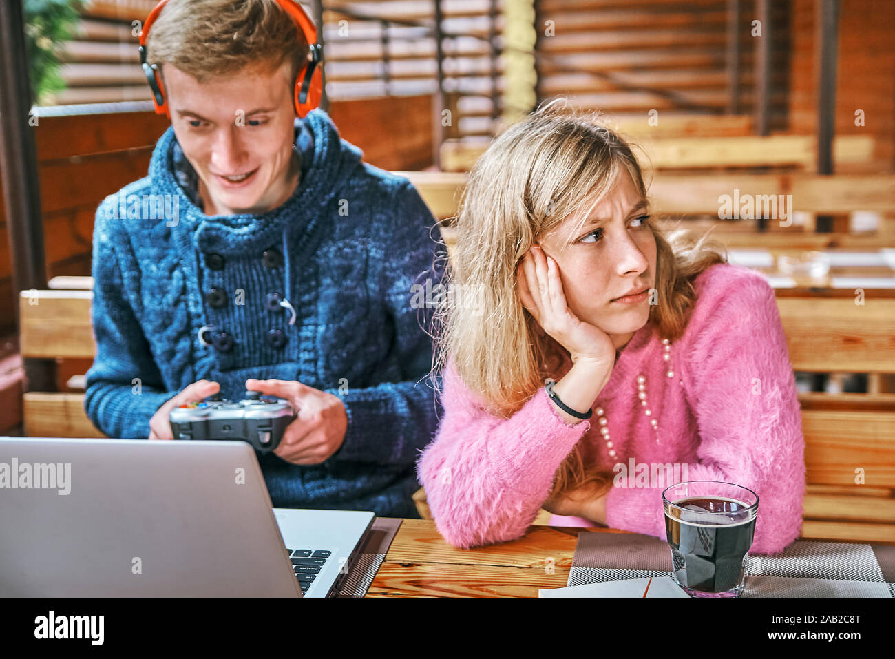 young guy plays games at a laptop in a cafe. the girl nearby is reading a book. wear concept Stock Photo