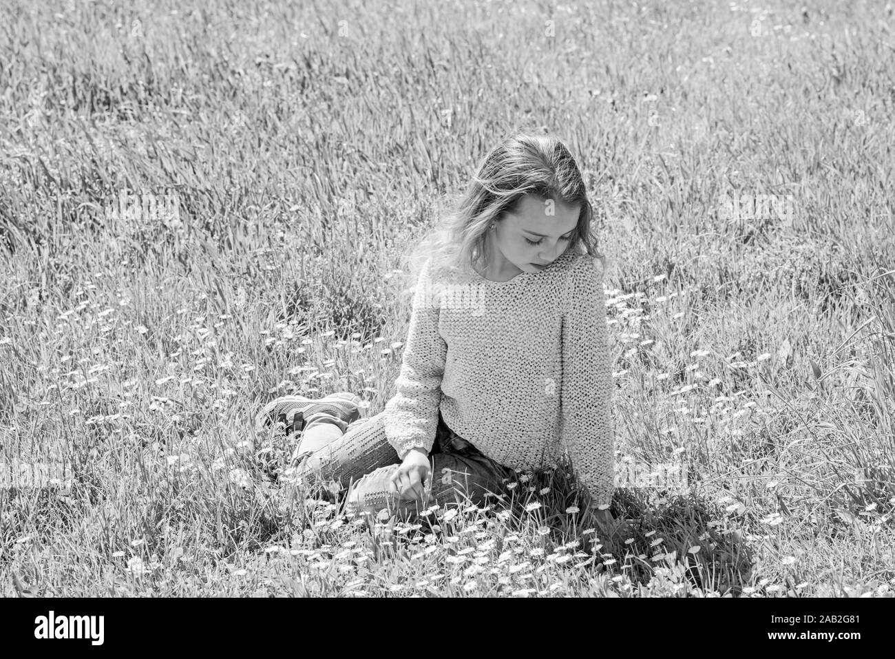 Girl on calm or sad face spend leisure outdoors. Girl sits on grass at ...
