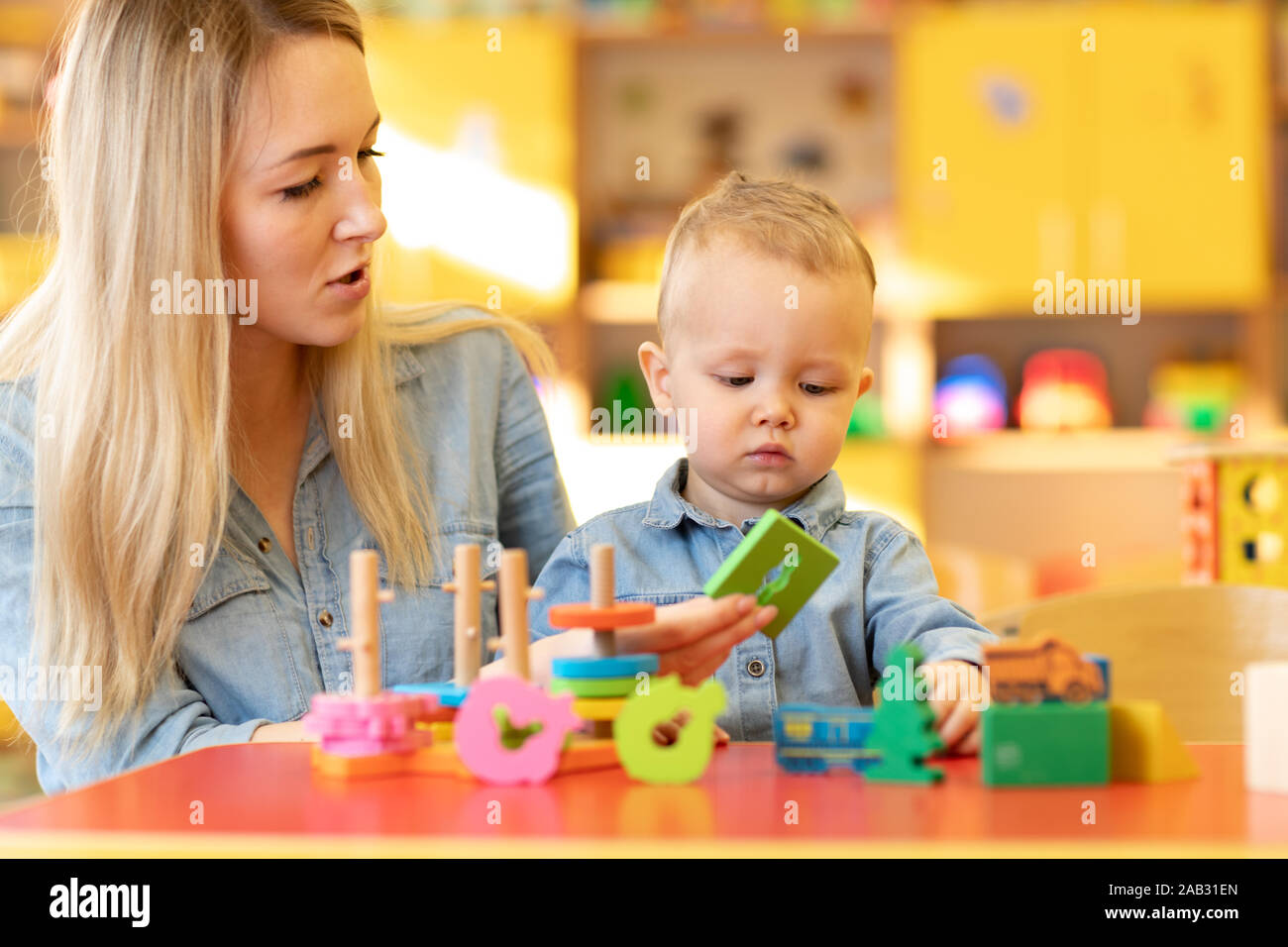 Nursery baby and carer play at table in kindergarten Stock Photo