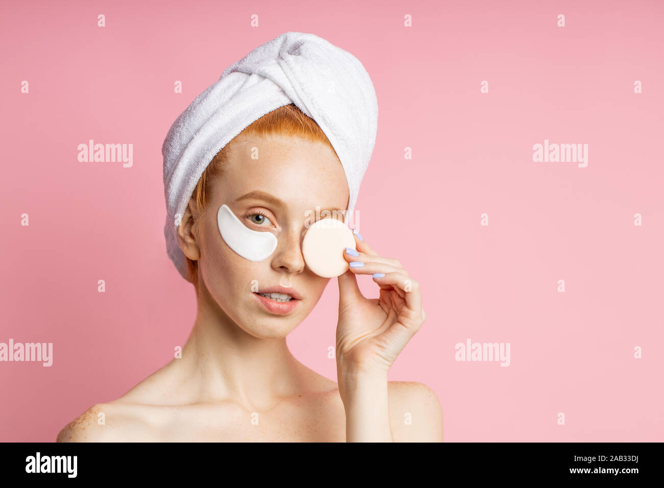 Attractive young redhead female model with fresh pure skin, towel on head, covering eye with