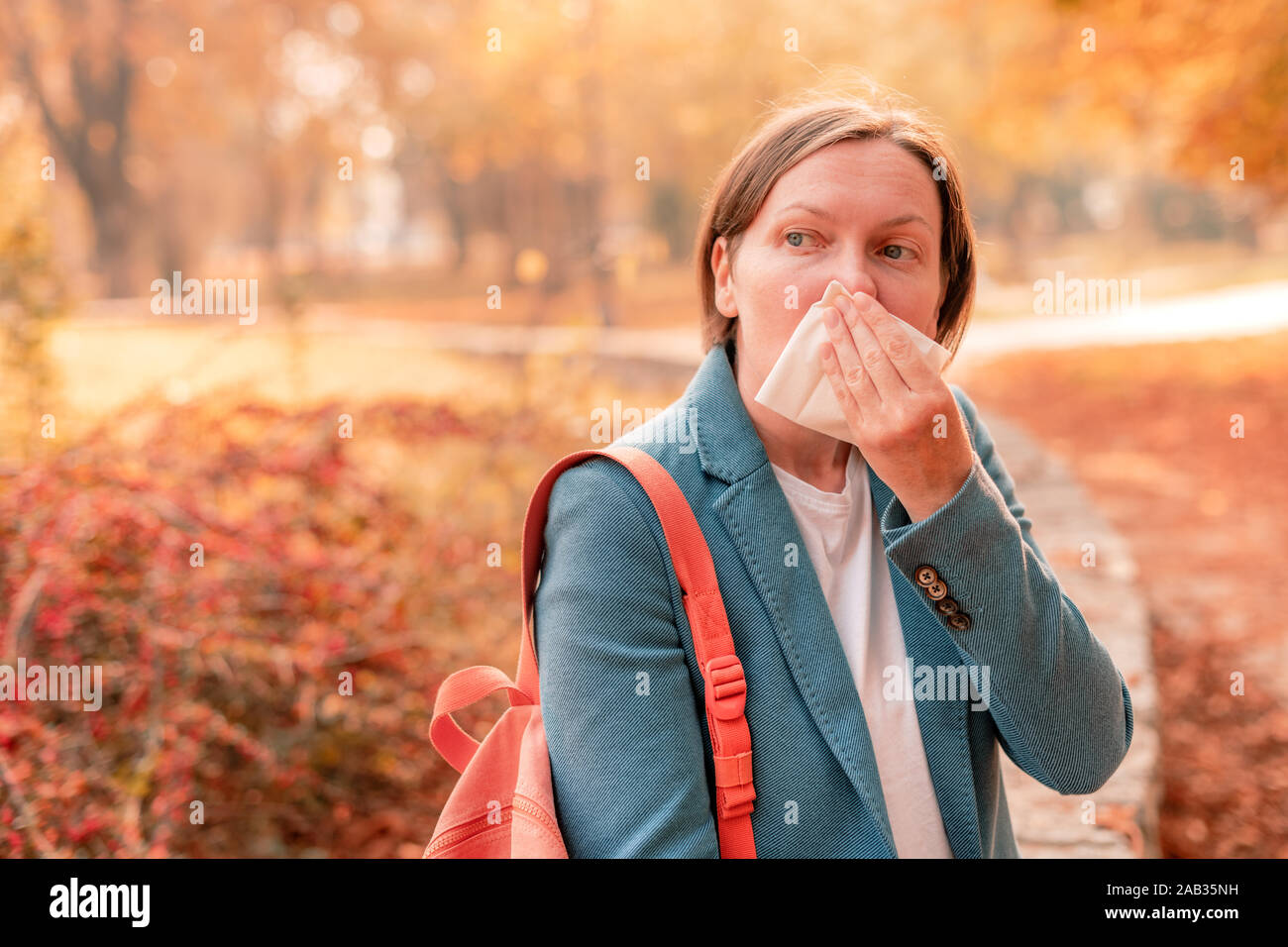 Businesswoman nose-blowing paper tissue in autumnal park during the work break, selective focus Stock Photo