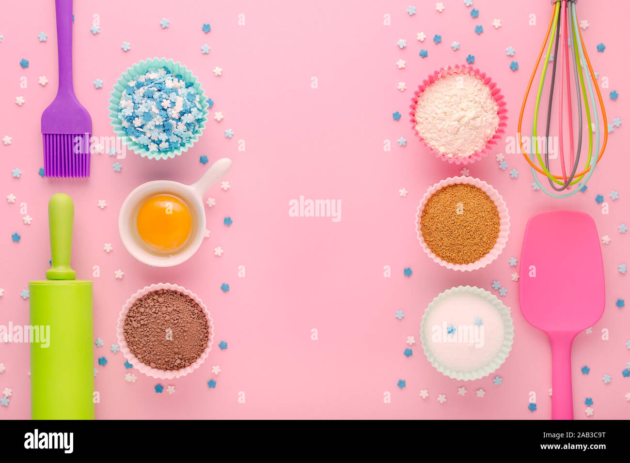 baking ingredients, egg, flour, cocoa, sugar, sweet decoration and kitchen tools on pink background Stock Photo