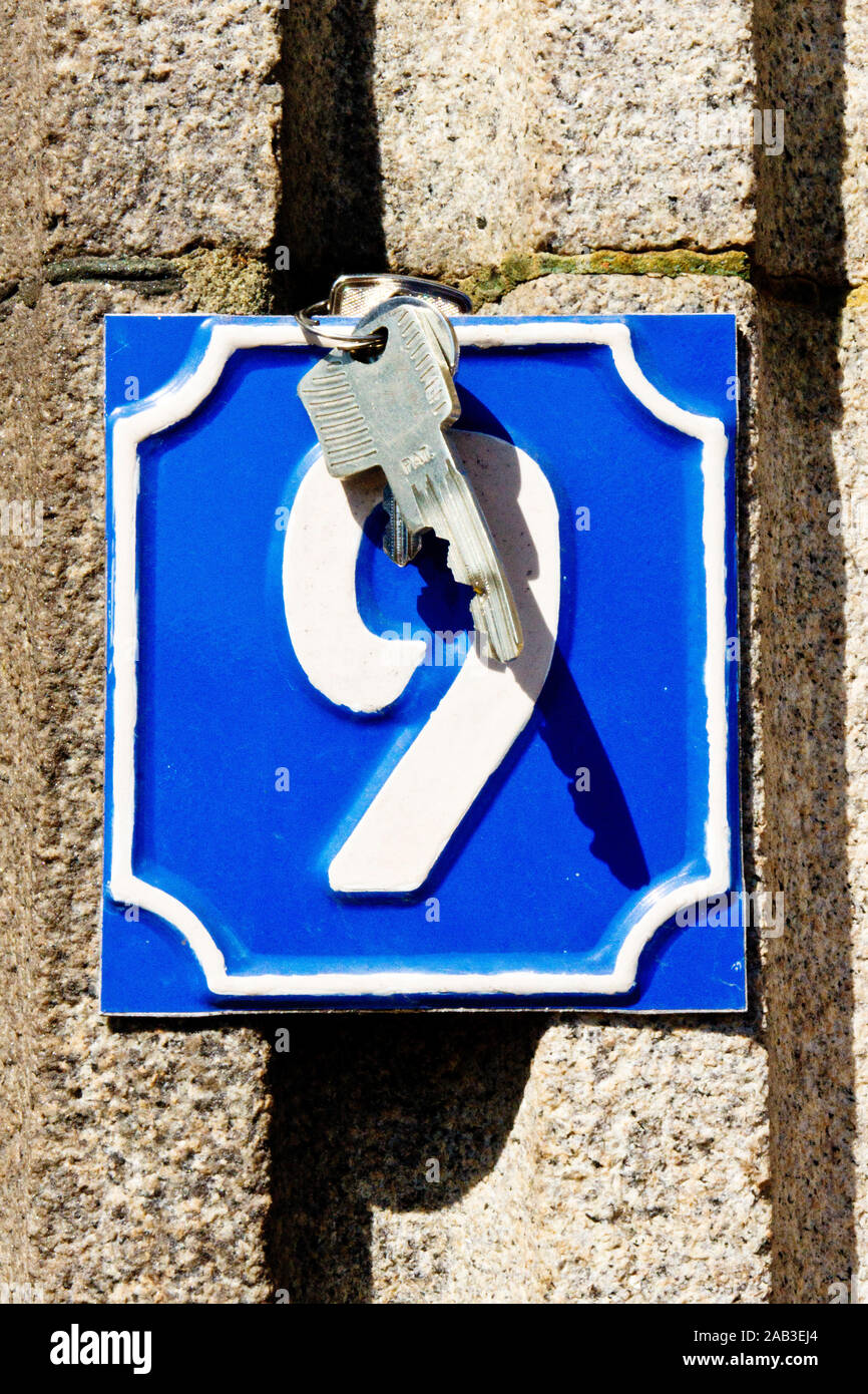 Schlüsselbund mit einem Haustürschlüssel hängt an einem Schild mit einer Hausnummer |Keychain with house keys hanging on a sign with a house number| Stock Photo