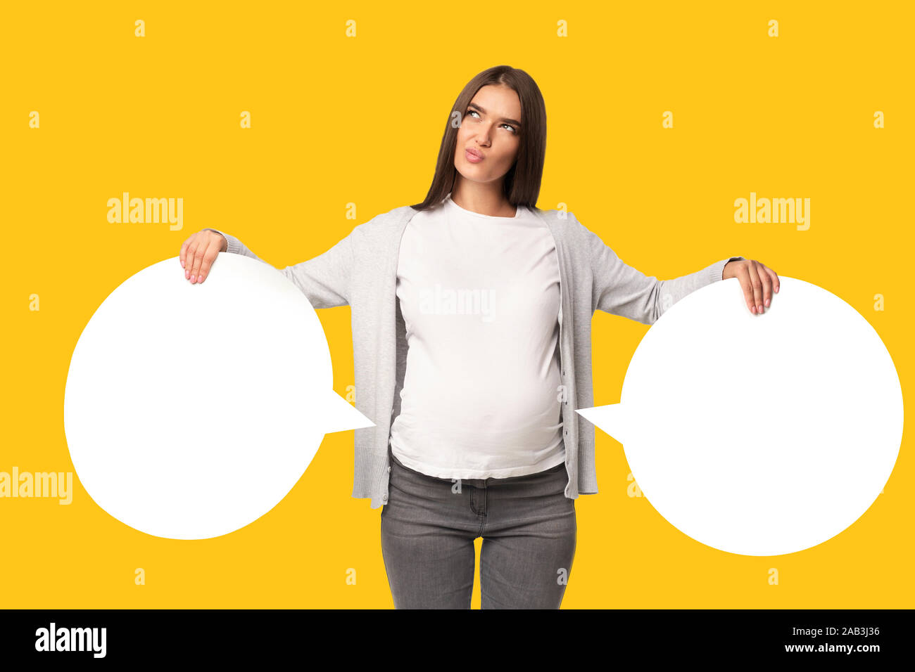 Pregnant Lady Holding Two Speech Bubbles Near Belly, Yellow Background Stock Photo
