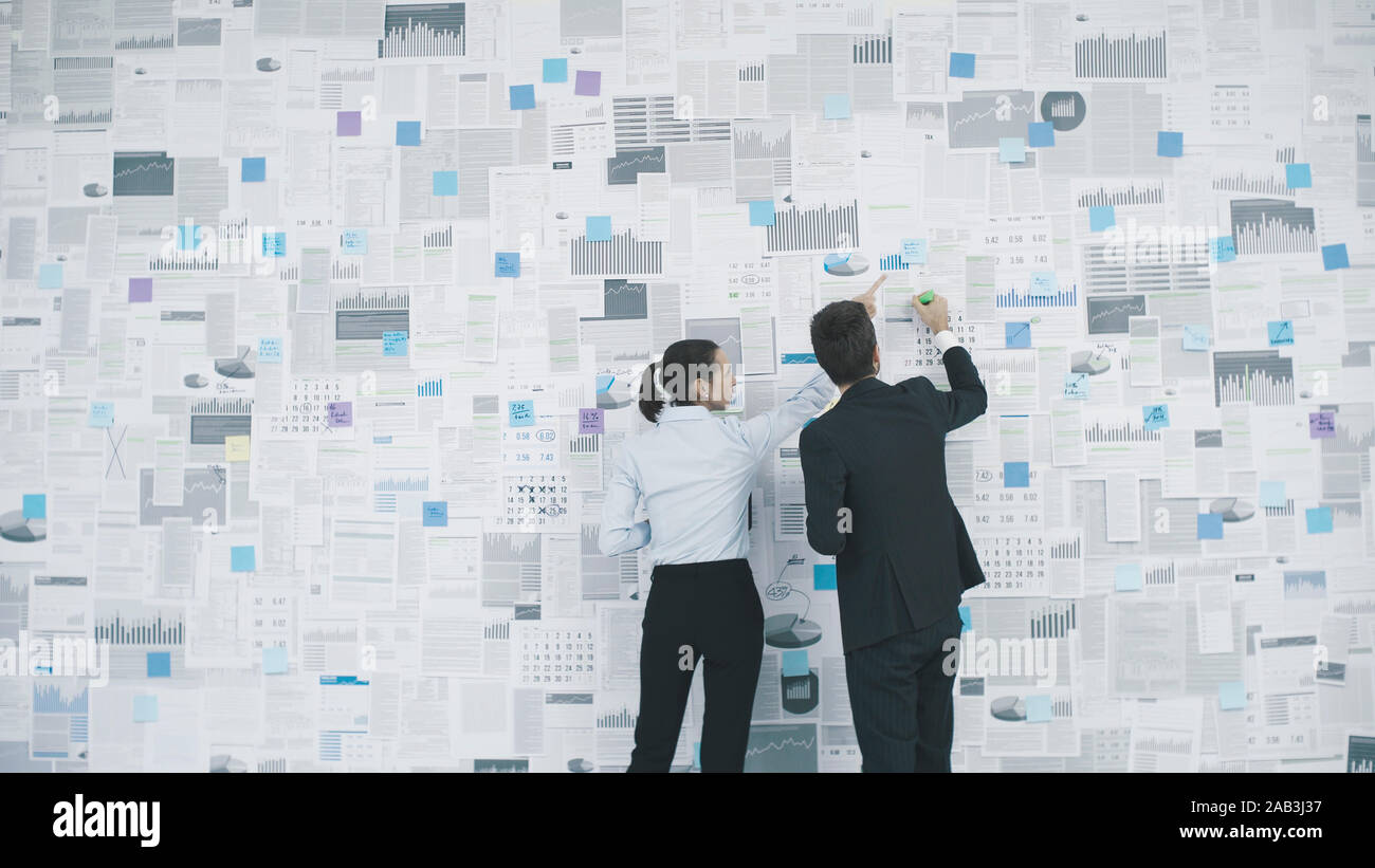 Corporate executives planning their business strategy: they are analyzing many financial reports and charts hanging on a wall Stock Photo