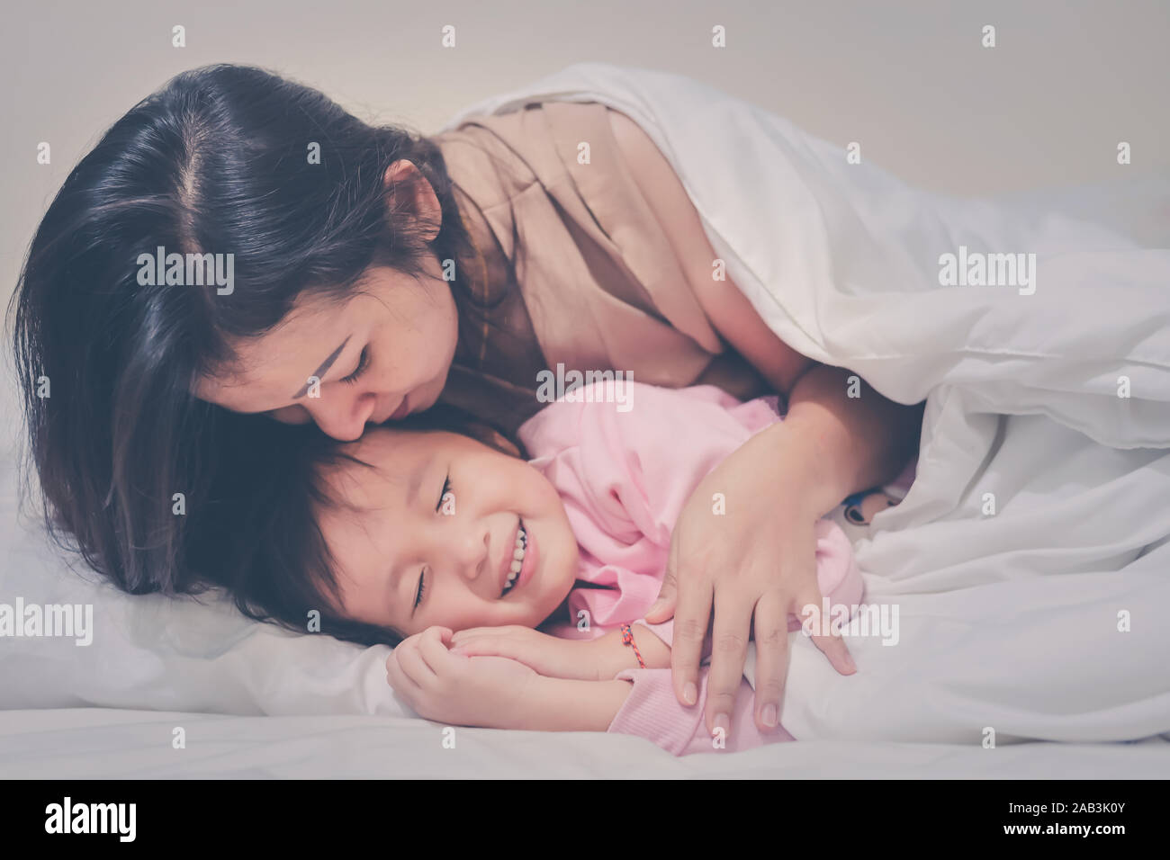 Mother gently kissing daughter wishing good night sweet dreams at night time soft focus happy family warm tone filter Stock Photo
