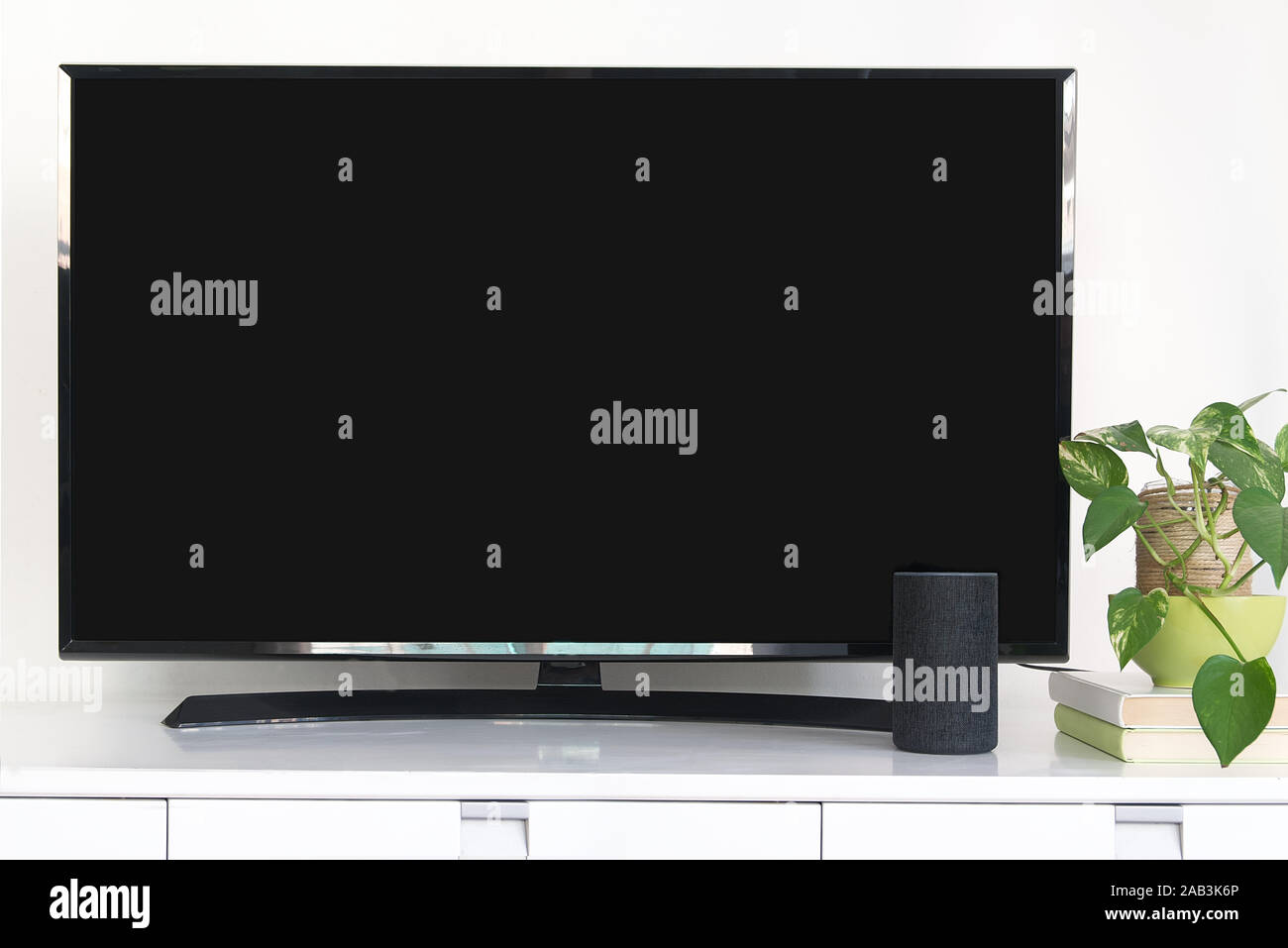 Alexa Echo Intelligent speaker device as home automation system to control a smart television. Living room with a black screen of a tv next to a plant. Stock Photo
