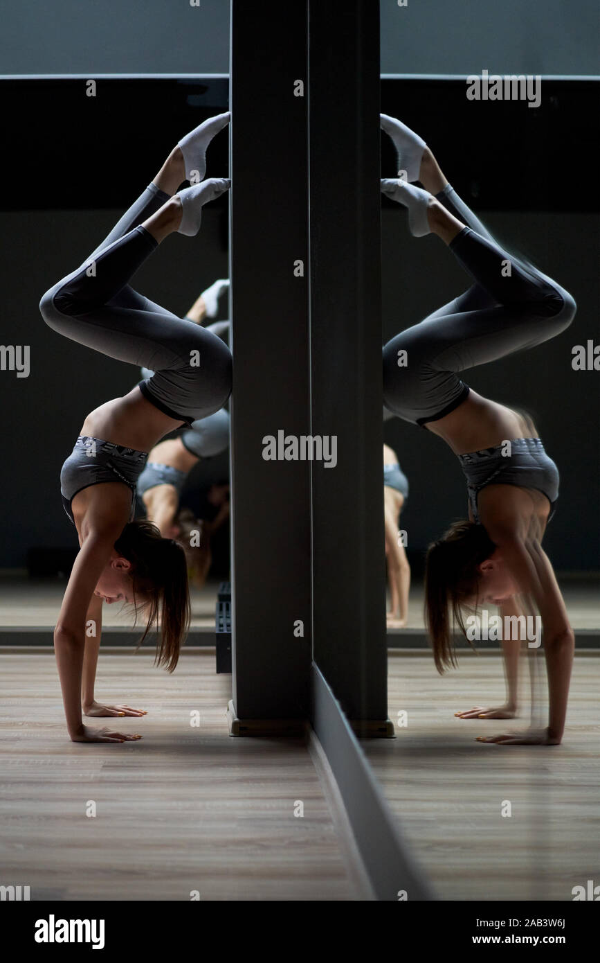 Sportwoman stands on her hands against gray wall in gym Stock Photo