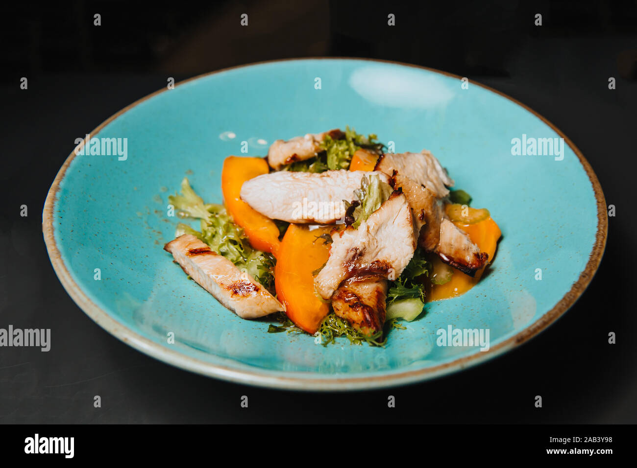 Meat, cooked grill, cut into pieces lies with vegetables on a round, blue plate. Stock Photo