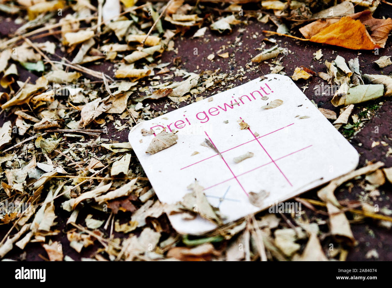 Ein Bierdeckel mit der Aufschrift „Drei gewinnt!“ liegt auf dem Gehweg |A beer mat that says 'Three wins!' Lying on the sidewalk| Stock Photo