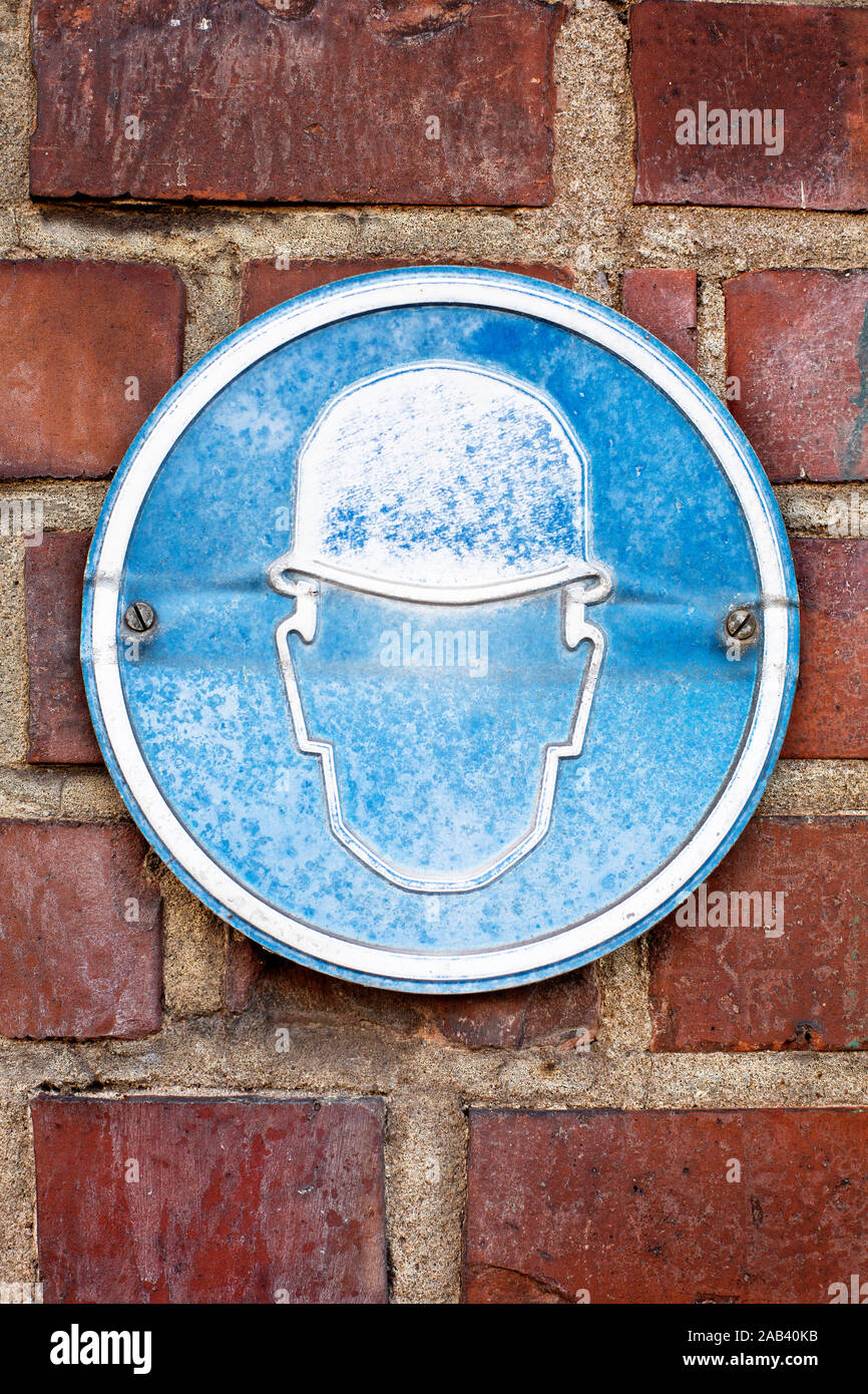 Ein ausgeblichenes Hinweisschild auf Helmpflicht  an einem Werksgelände |A faded sign helmet are mandatory on at a plant site| Stock Photo