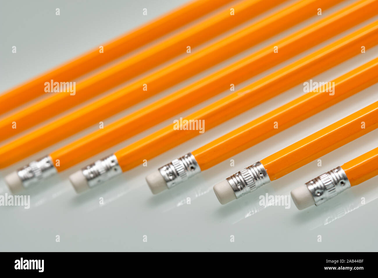 Background with a pattern consisting of a closeup of a row of orange lead pencils with white rubbers on the end lying on a white glass plate. Stock Photo