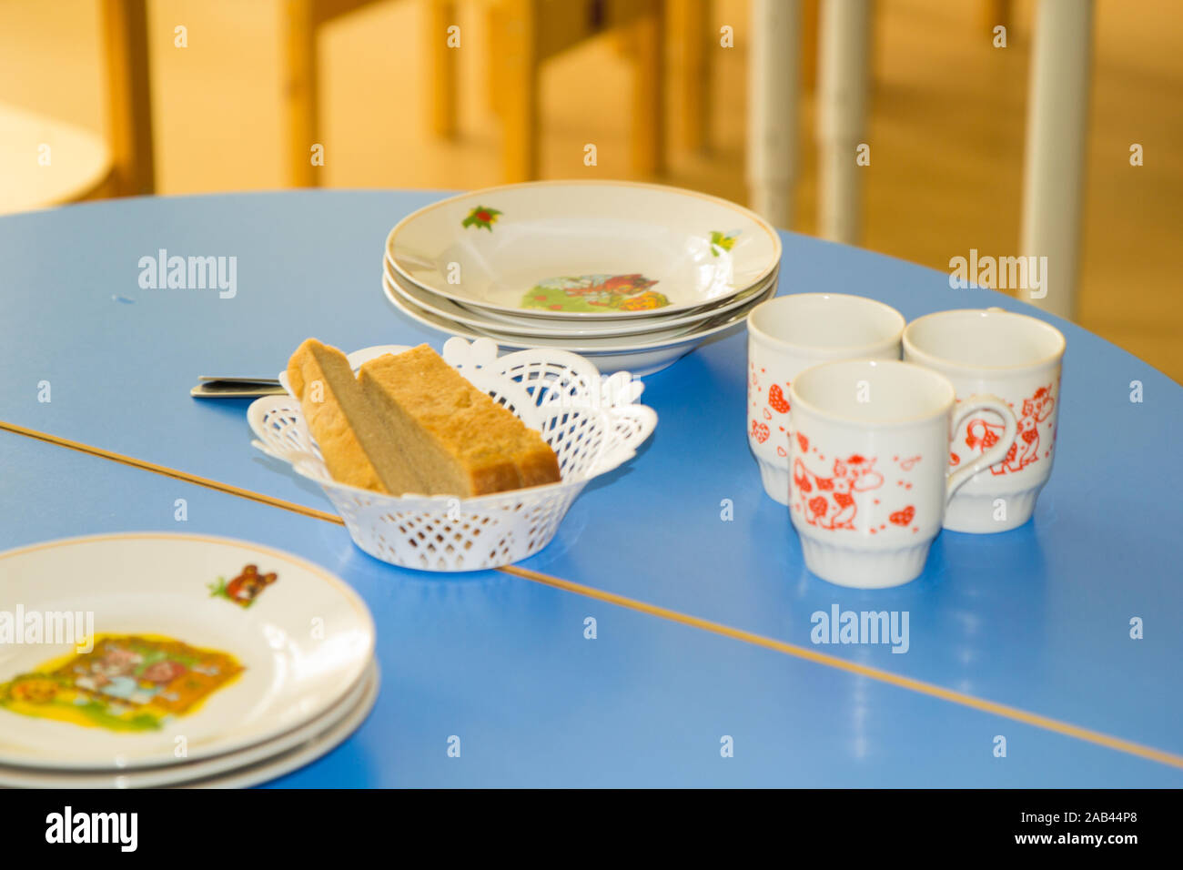 Served dinner table for children with bread, plates with illustrations. Colorful child table. Kinder garden at lunch time. Stock Photo