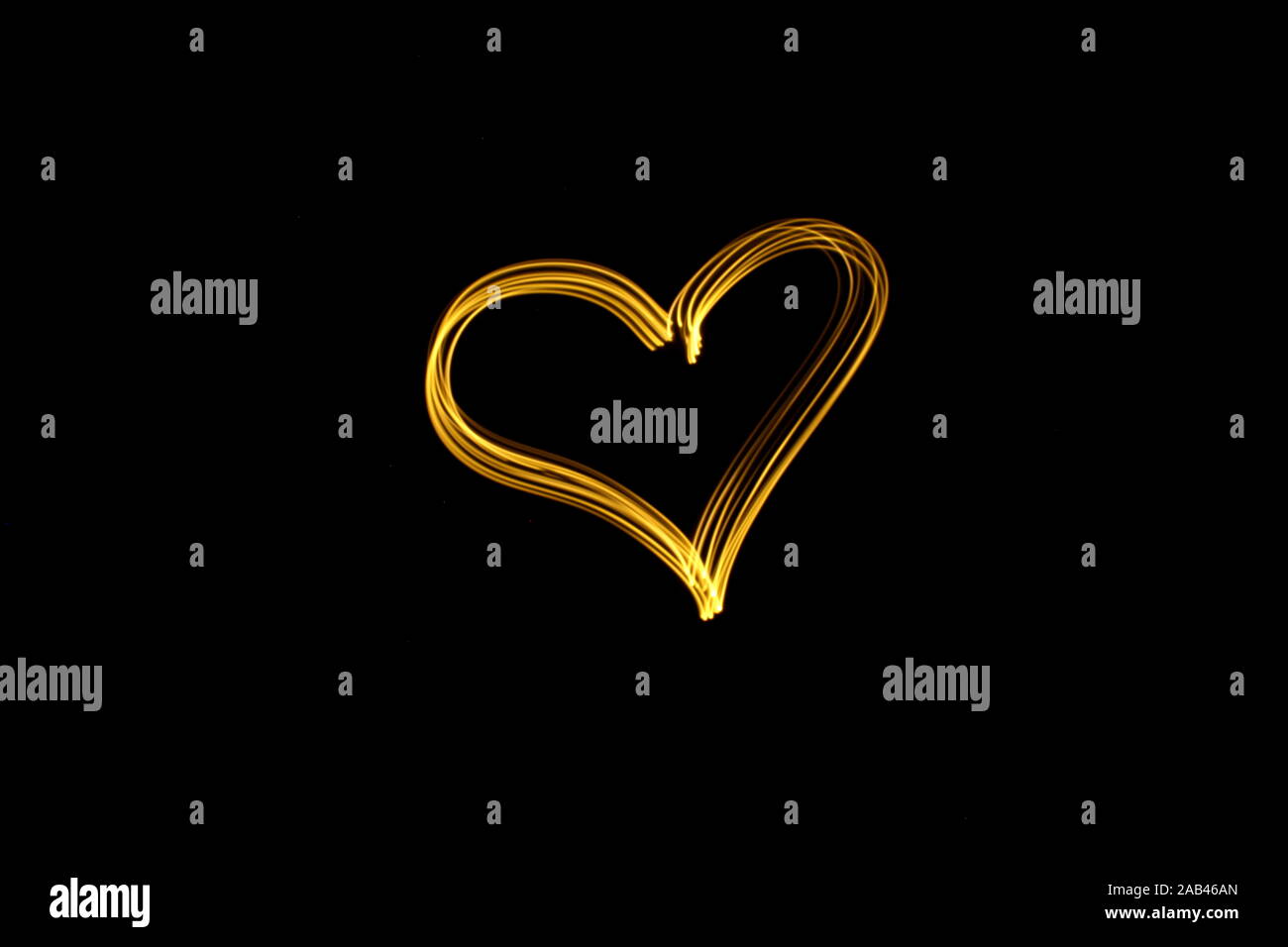 Long exposure photograph of neon gold color in a heart outline shape, against a black background. Light painting photography. Love, romance concept Stock Photo