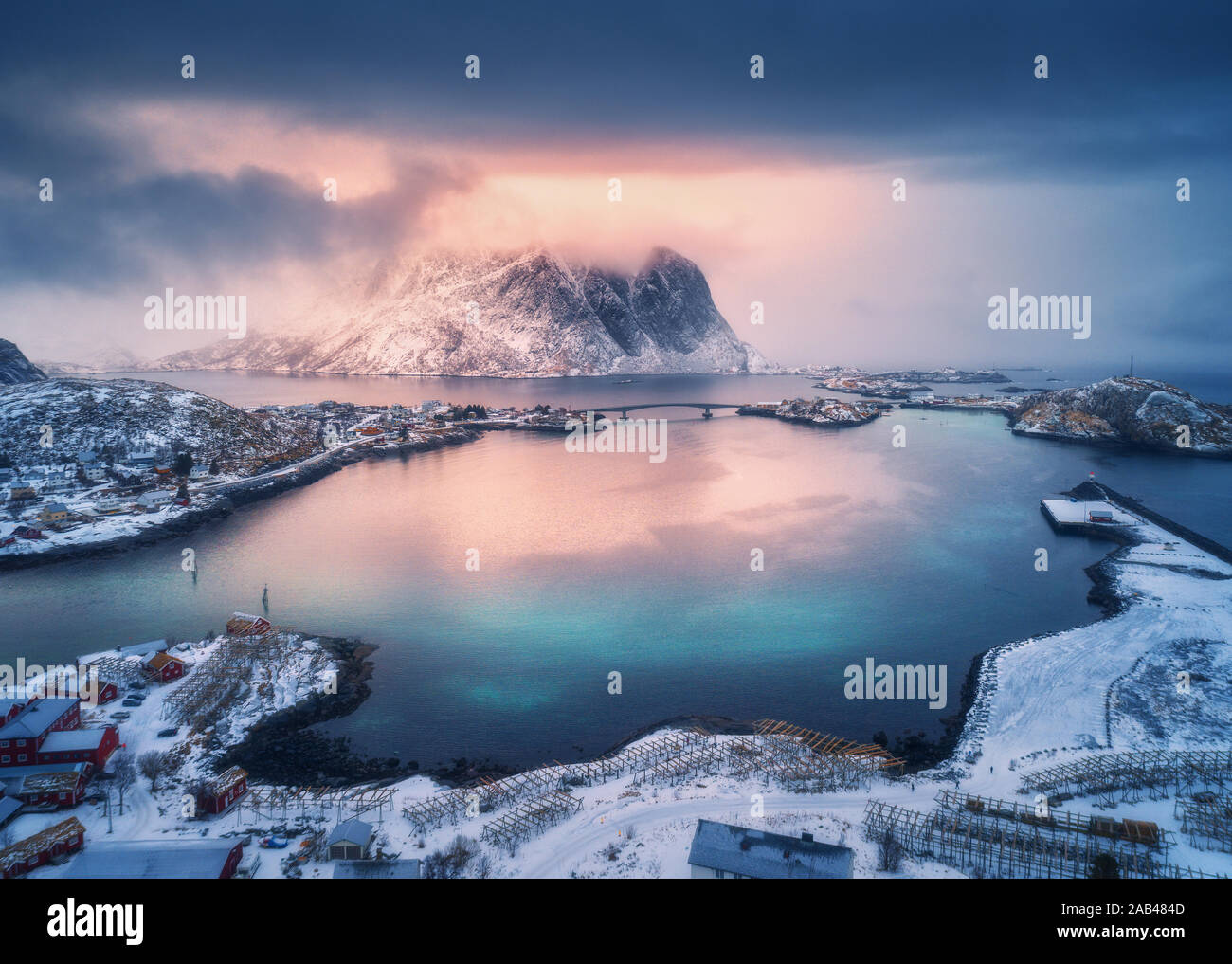 Aerial view of snowy mountain, village on sea coast, colorful sky Stock Photo