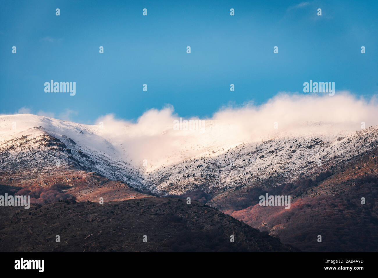 Last hours of the day with snowy mountain hills with white puffy clouds and blue sky Stock Photo