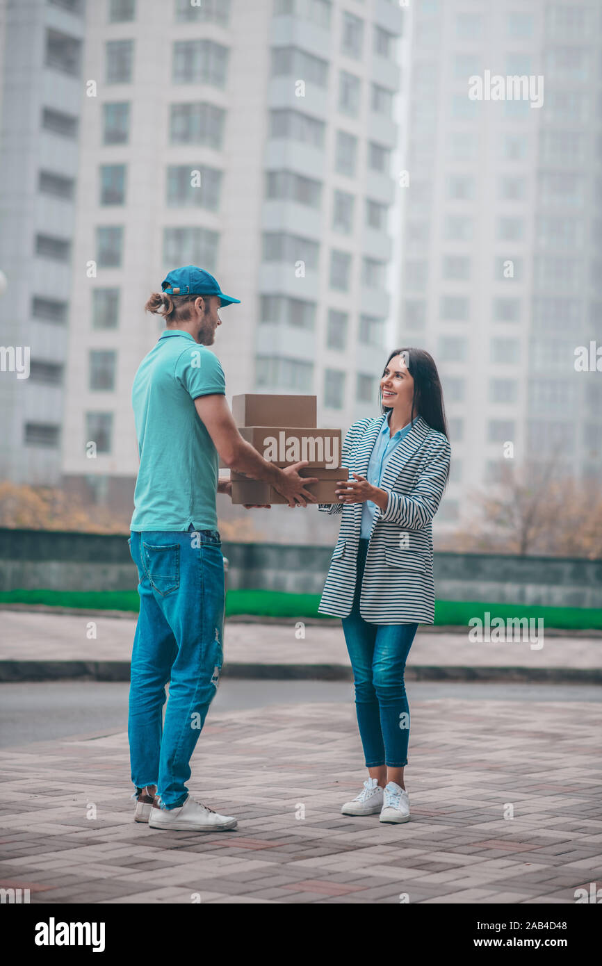 Man Giving Box Delivery man giving boxes to woman while meeting her in the street ...