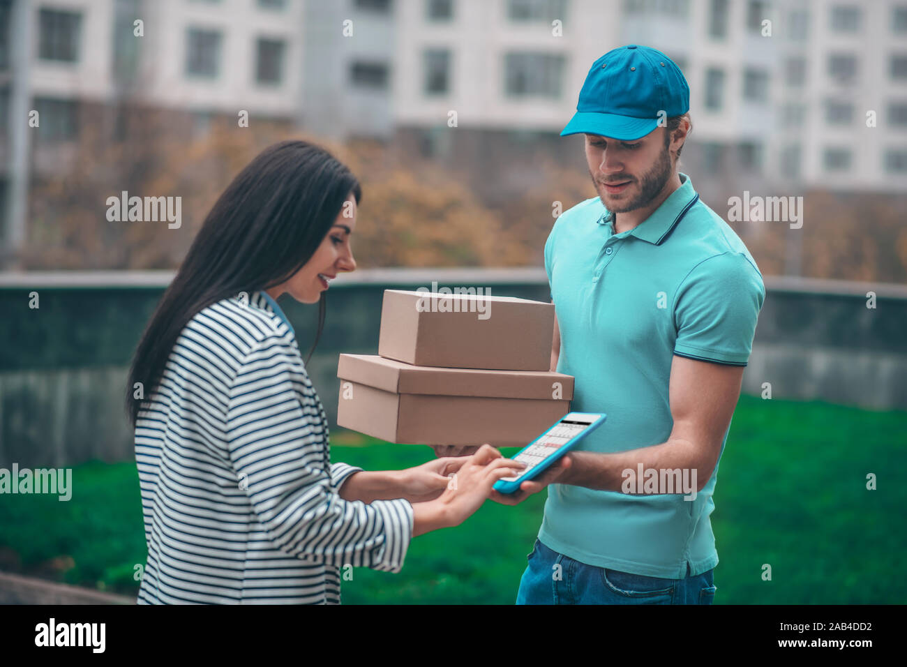 Dark-haired woman standing near delivery man holding boxes Stock Photo