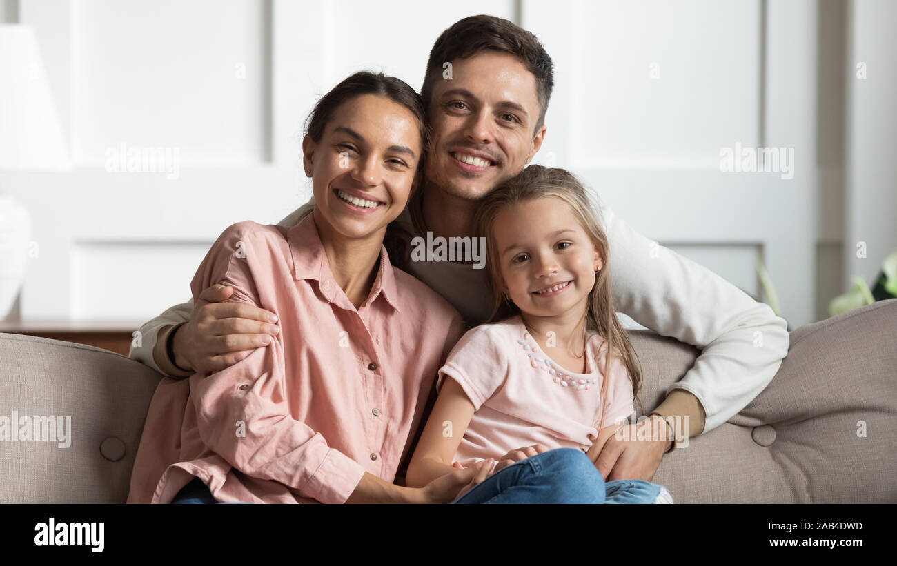 Beautiful young parents with small daughter sit on sofa, portrait Stock Photo