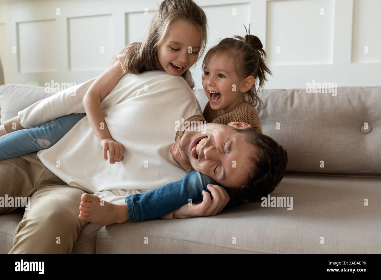 Funny young father playing with cute little children on sofa Stock Photo
