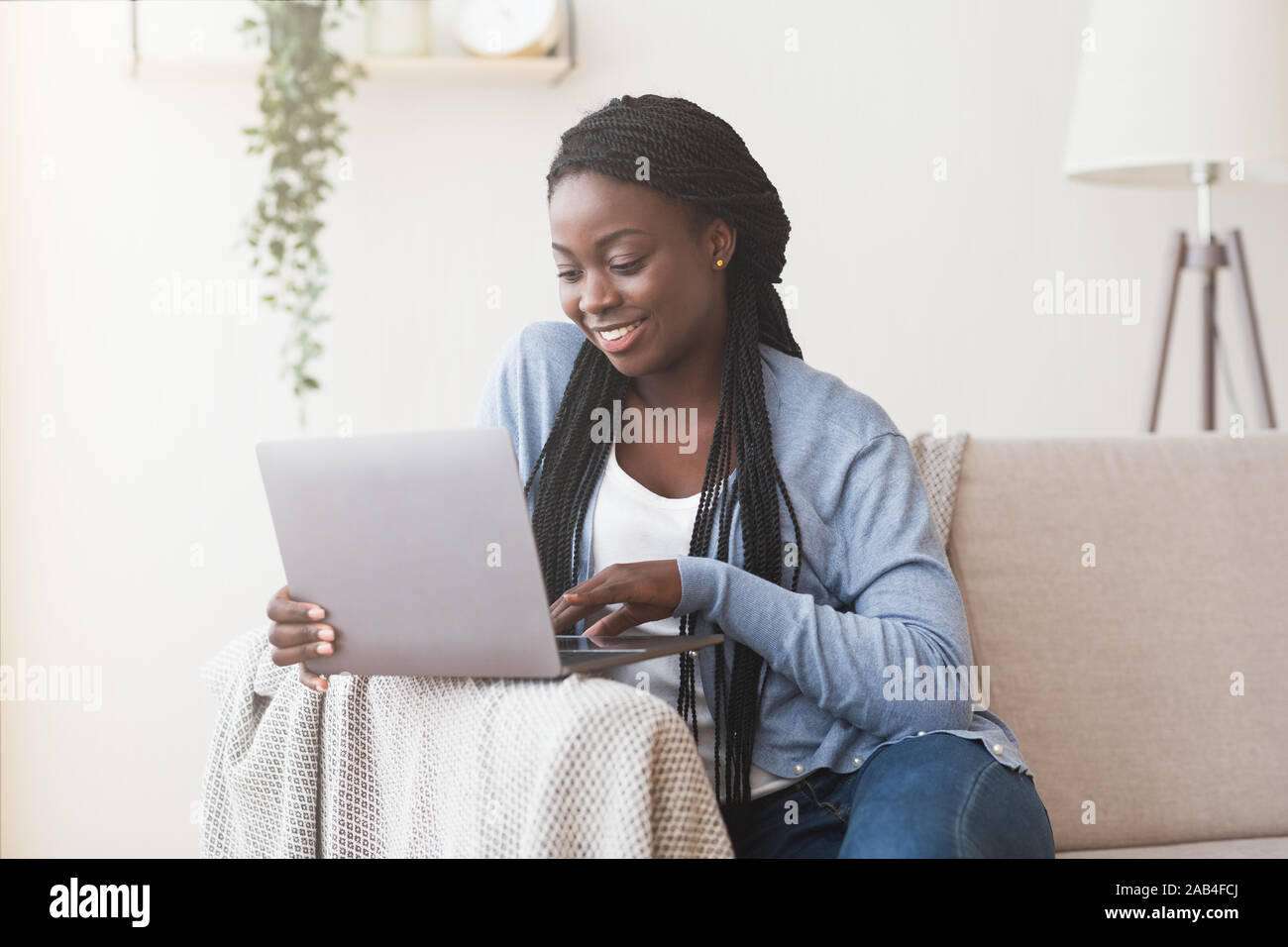 Young black woman working with laptop on sofa at home Stock Photo - Alamy