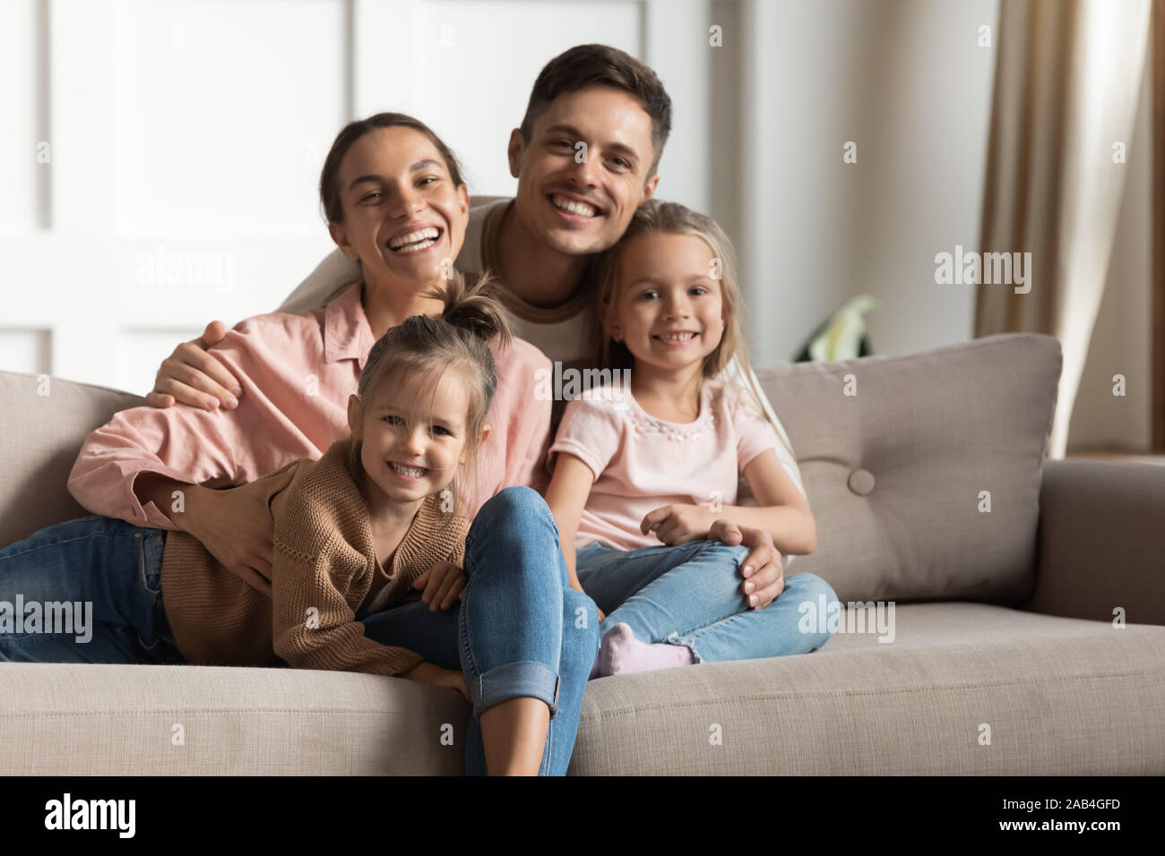 Smiling parents hug small kids daughters relaxing on couch, portrait Stock Photo