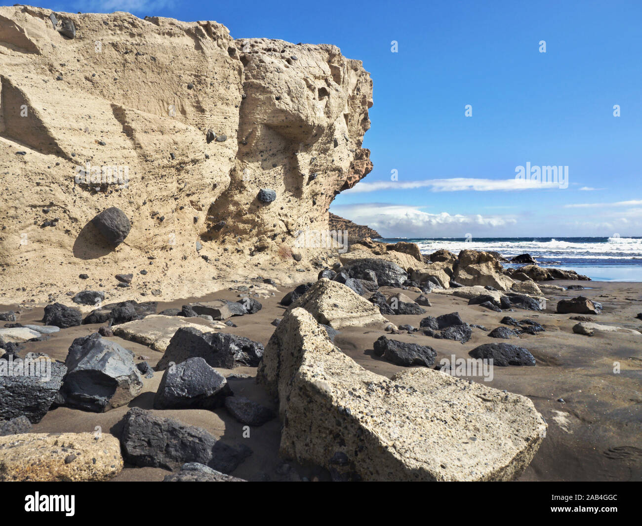 Extreme tuff and lava information on a beach on Tenerife. A high tufa wall on the left and fallen tufa boulders and black lava stones lie on the beach Stock Photo