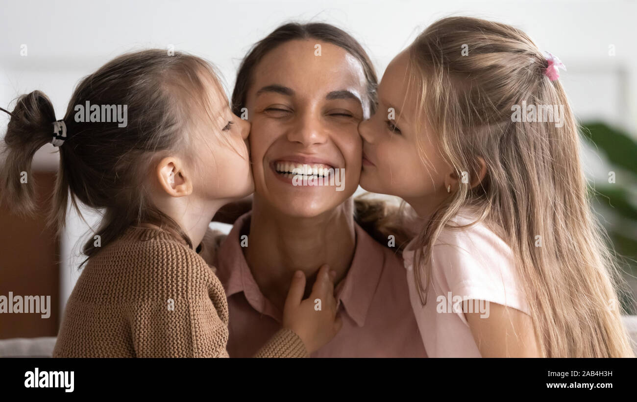 Two cute adorable little daughters kissing happy mum on cheeks Stock Photo