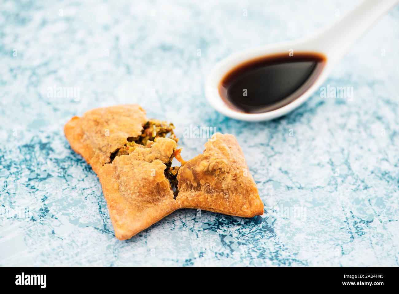 high angle view of an open Indian samosa and a ceramic spoon with a dark sauce on a marbled stone surface Stock Photo