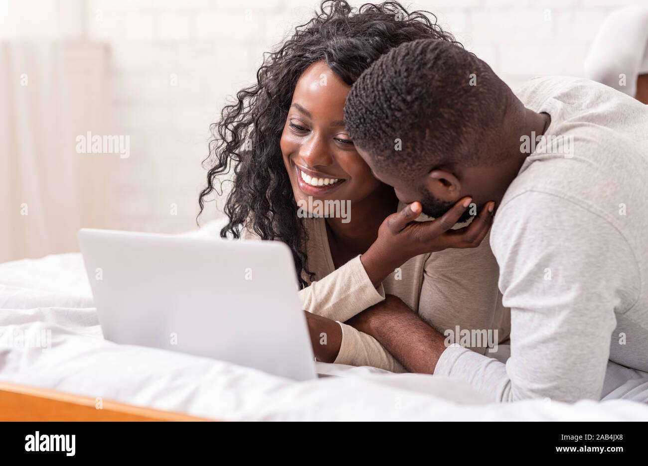 Cheeful african american couple relaxing on bed with laptop Stock Photo ...