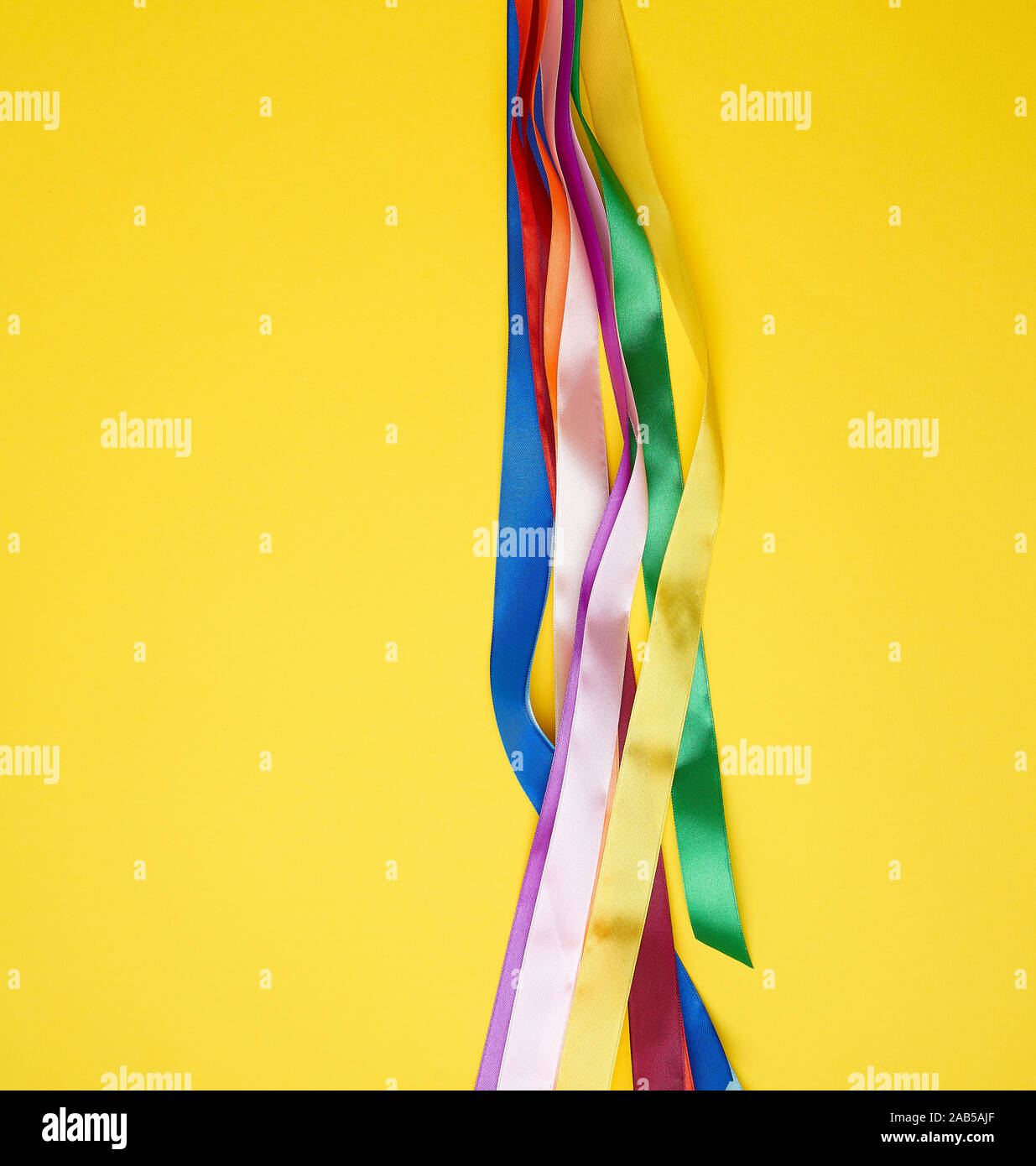 many silk multi-colored ribbons on a yellow background, top view Stock Photo
