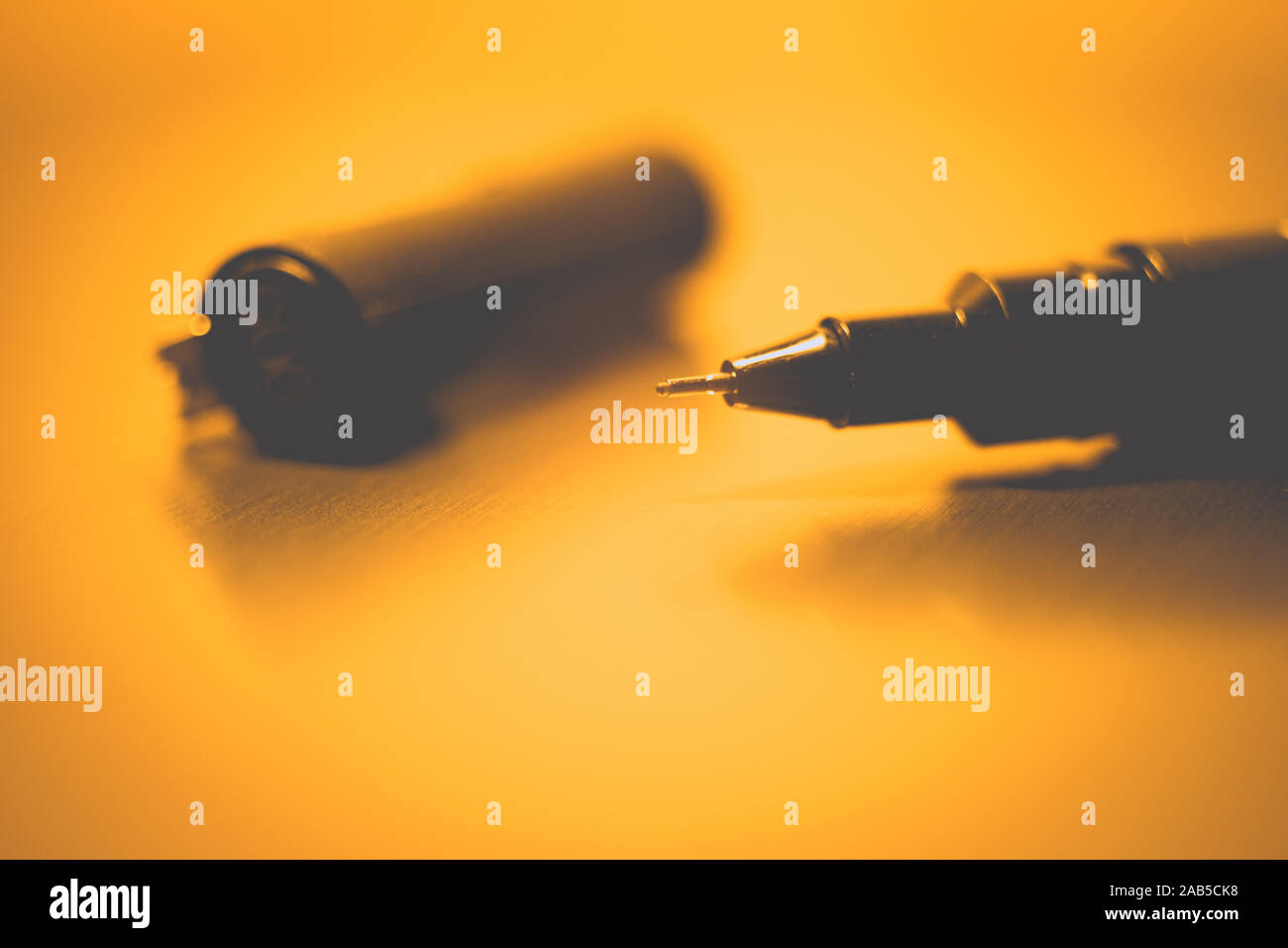 Black pen on a orange notebook paper, accessory for creativity on the table. Stock Photo