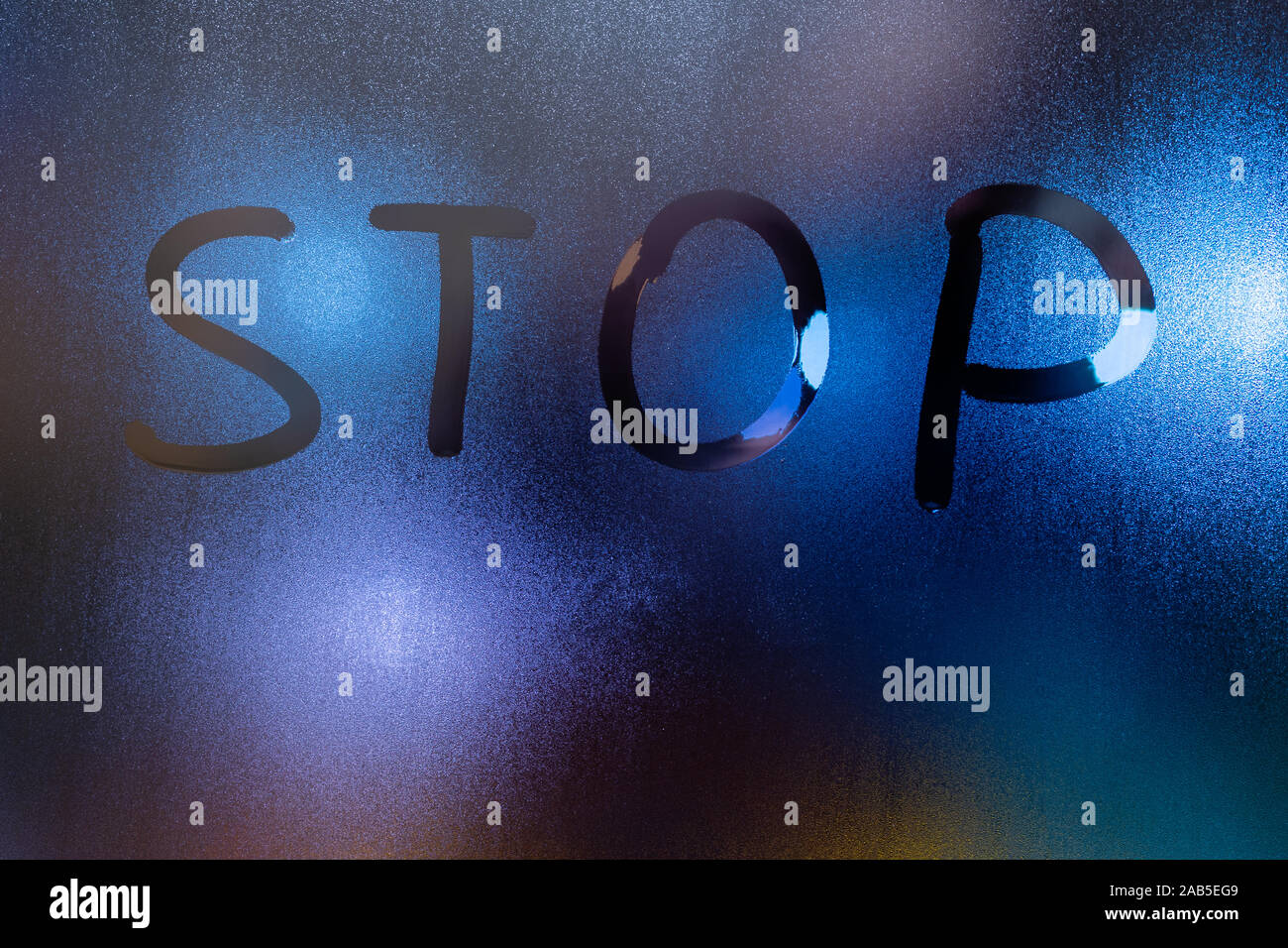 the word stop written on night wet window glass close-up with blurred background. Stock Photo
