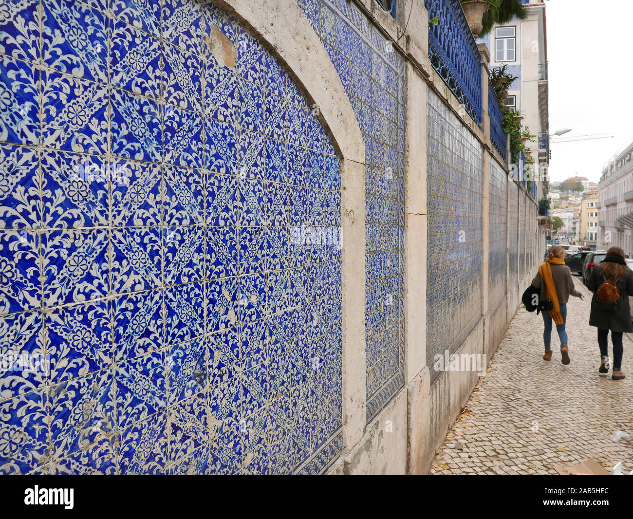 Blue and white tiling on the side of a building in the Santos area of lisbon Portugal with two people walking along the pavement alongside Stock Photo