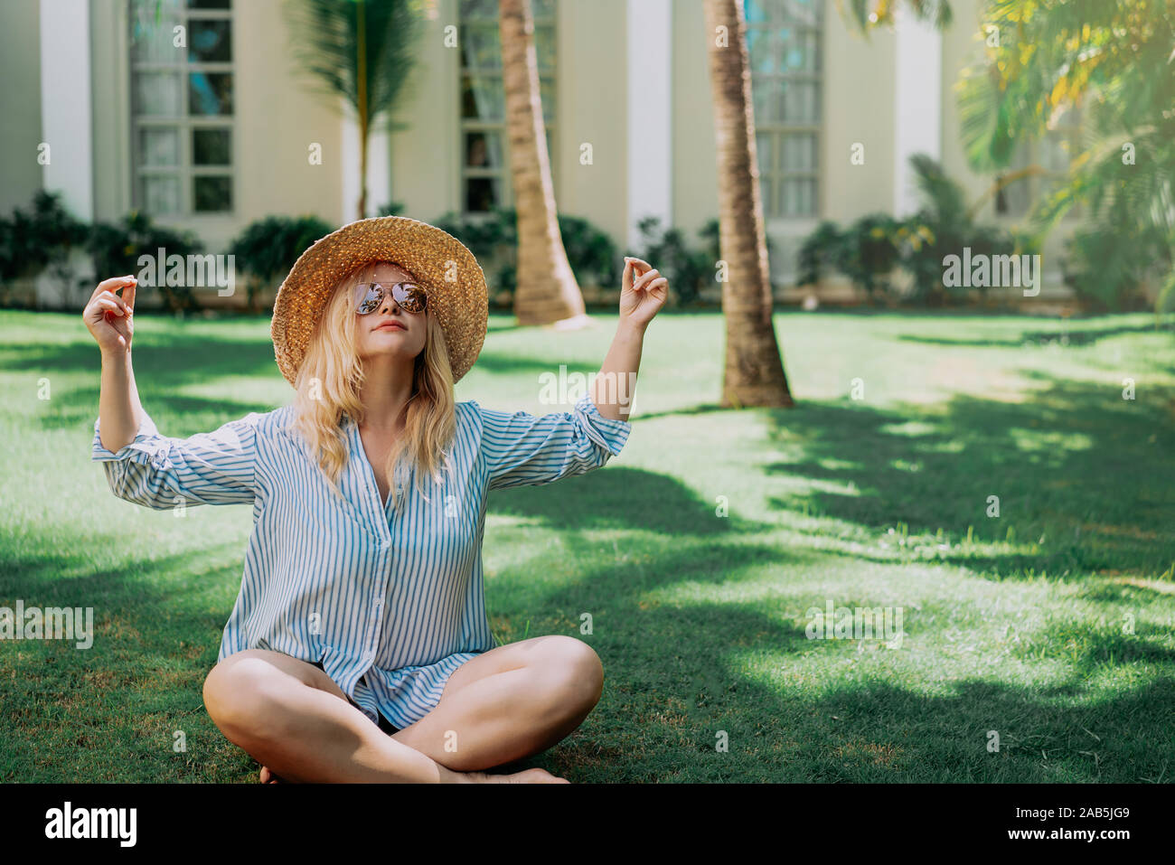 Portrait of beautiful of traveler woman with hat doing yoga behind palm trees. Sunlight. Concept travel, vacation, dream,sport Stock Photo