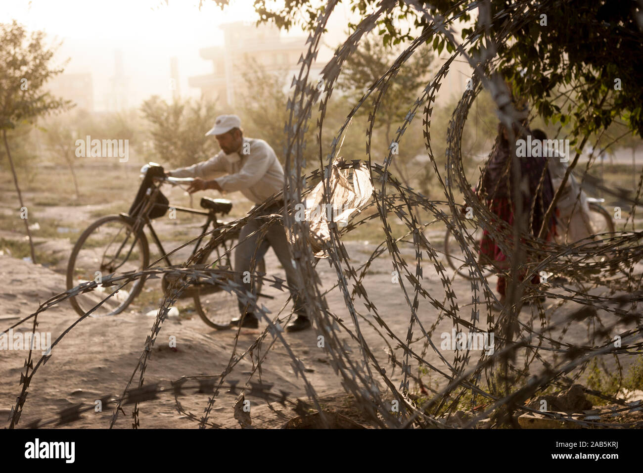 A man pushes his bicycle on the other side of coils of barbed wire laid along a frquently used path in Kabul, Afghanistan Stock Photo