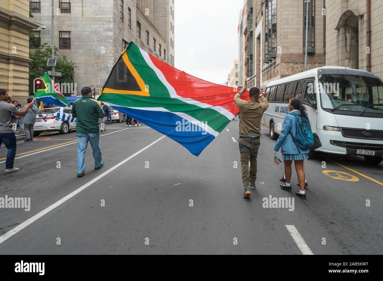 people walk in the city street of Cape Town holding up a big South African national flag to celebrate the victory of the national rugby team Stock Photo