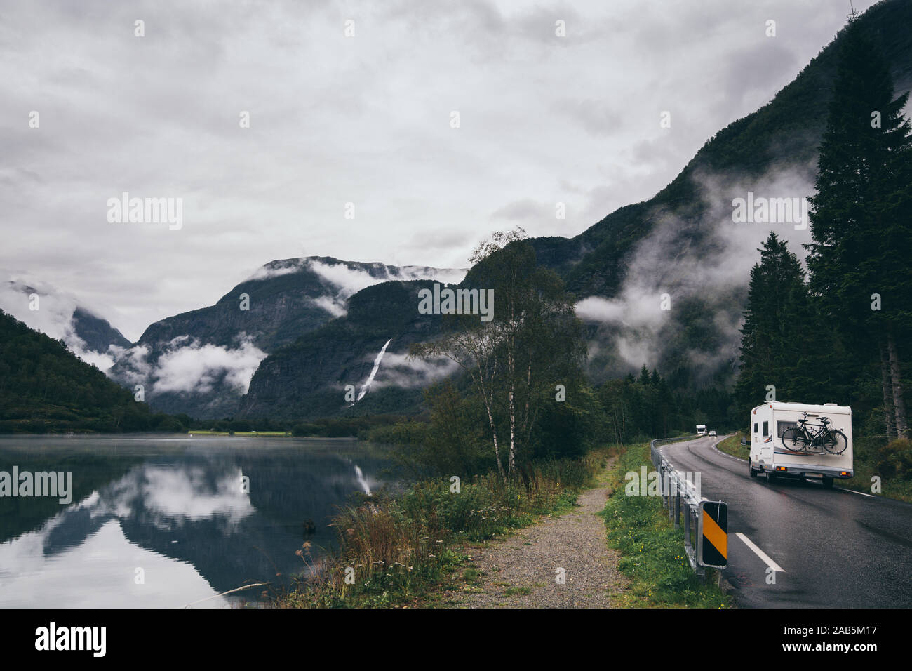 Campervan driving along Geiranger fjord in Norway, mountain reflection in water. Stock Photo
