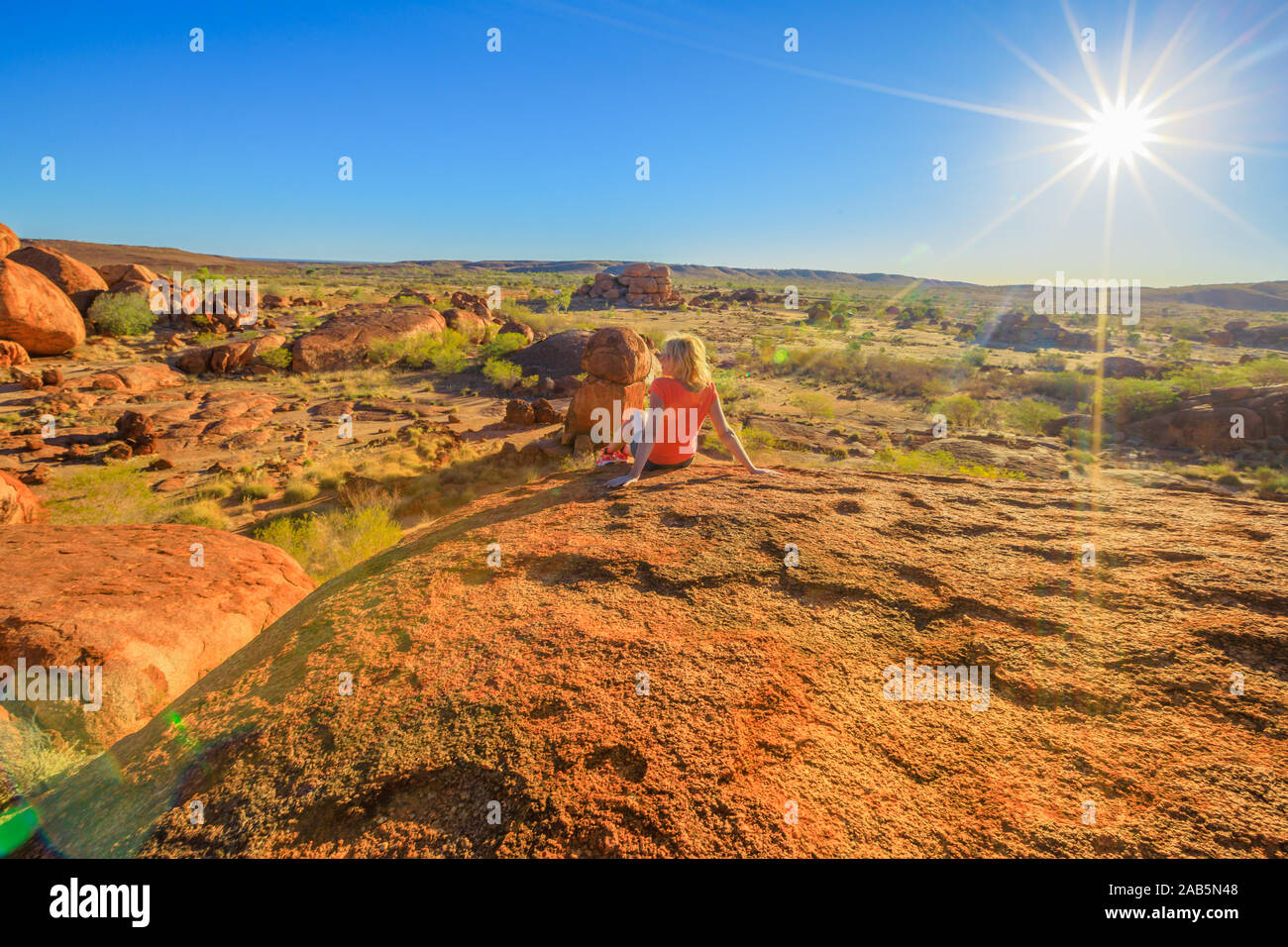 Tourist woman on the top of Karlu Karlu Devils Marbles Conservation Reserve looking panoramic views of granite boulders rock formations at sunset with Stock Photo